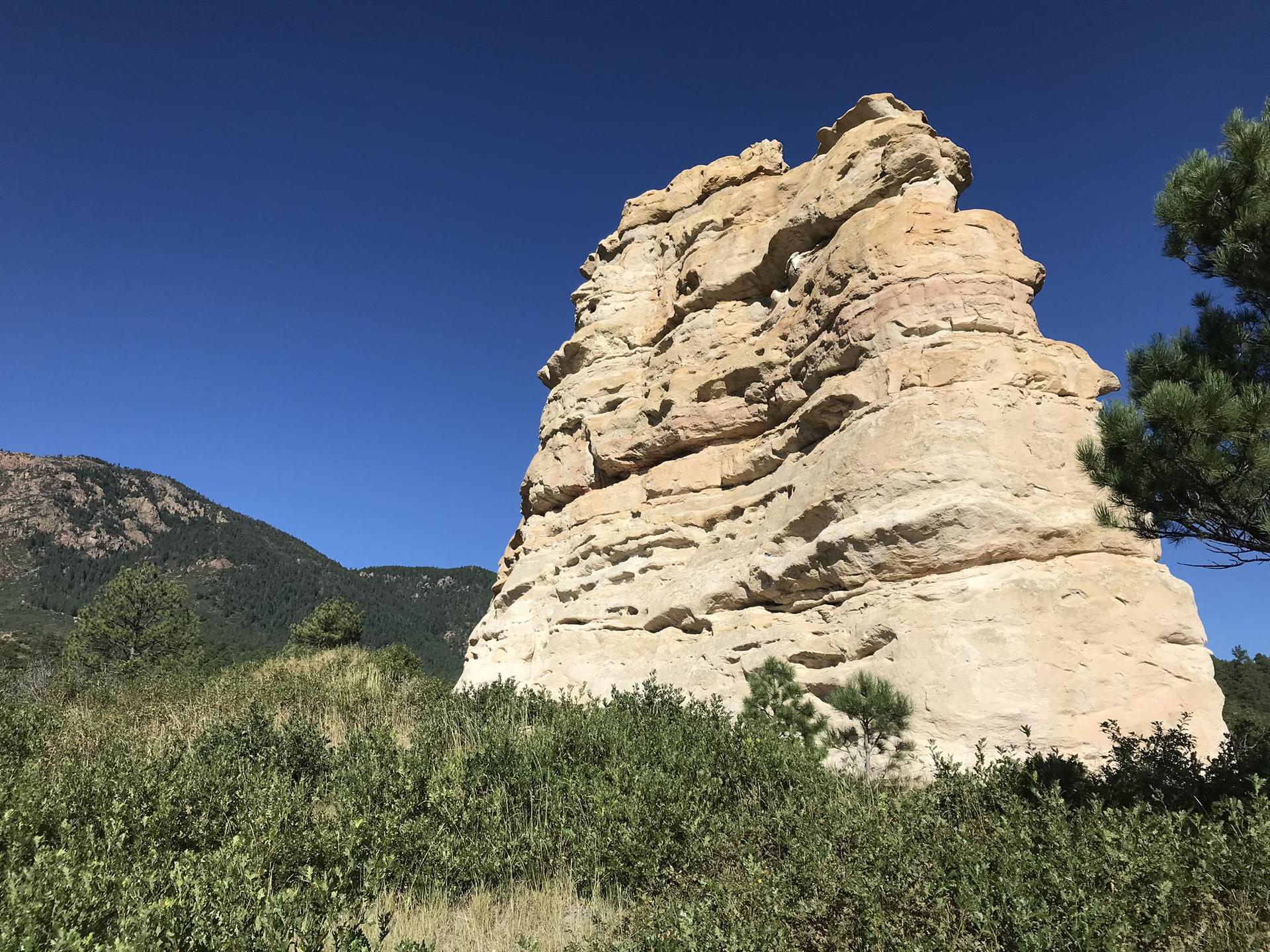 Large, light-colored rock formation stands tall under a clear blue sky.