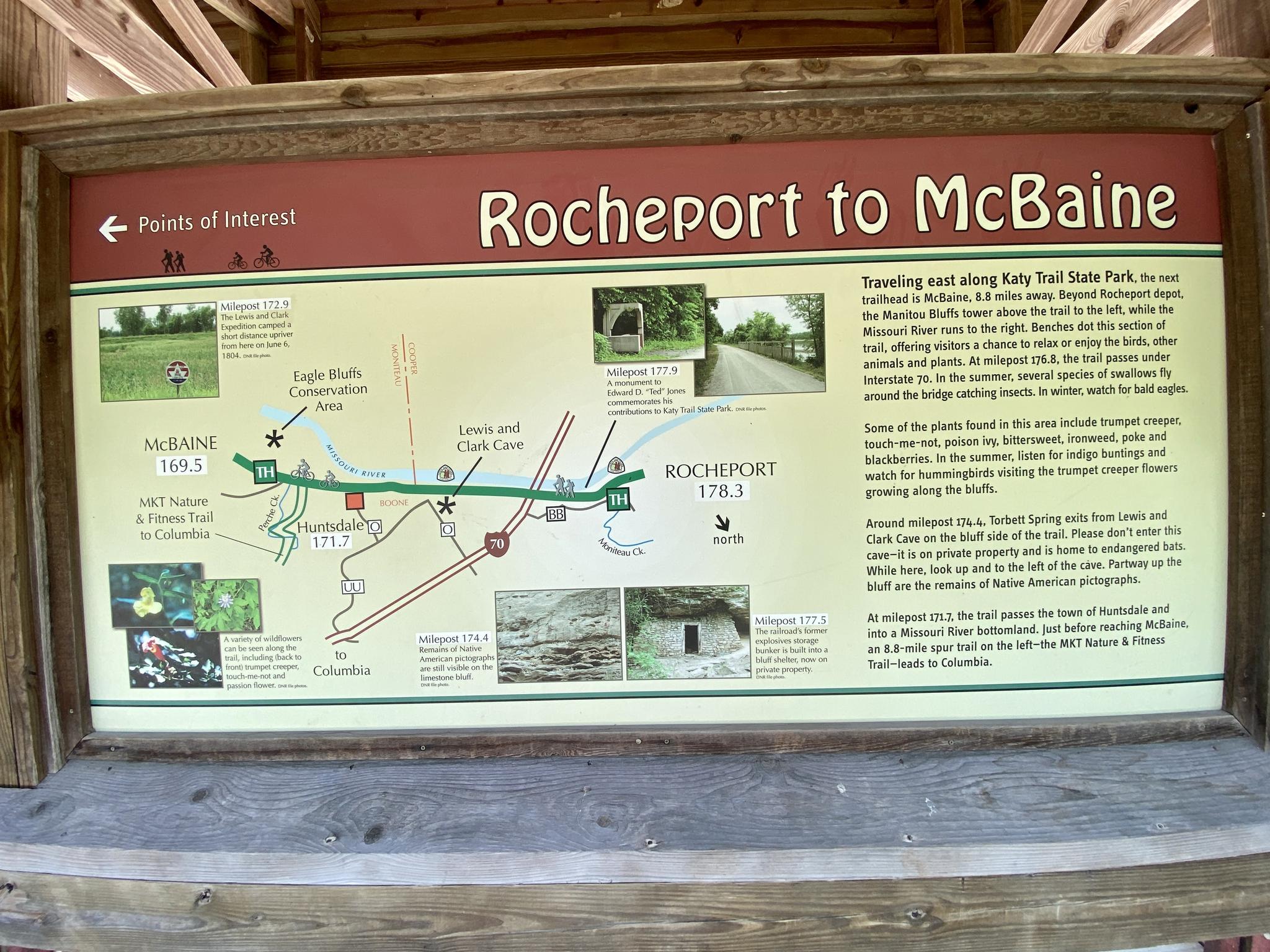 An outdoor information sign with a map and text under a wooden shelter.