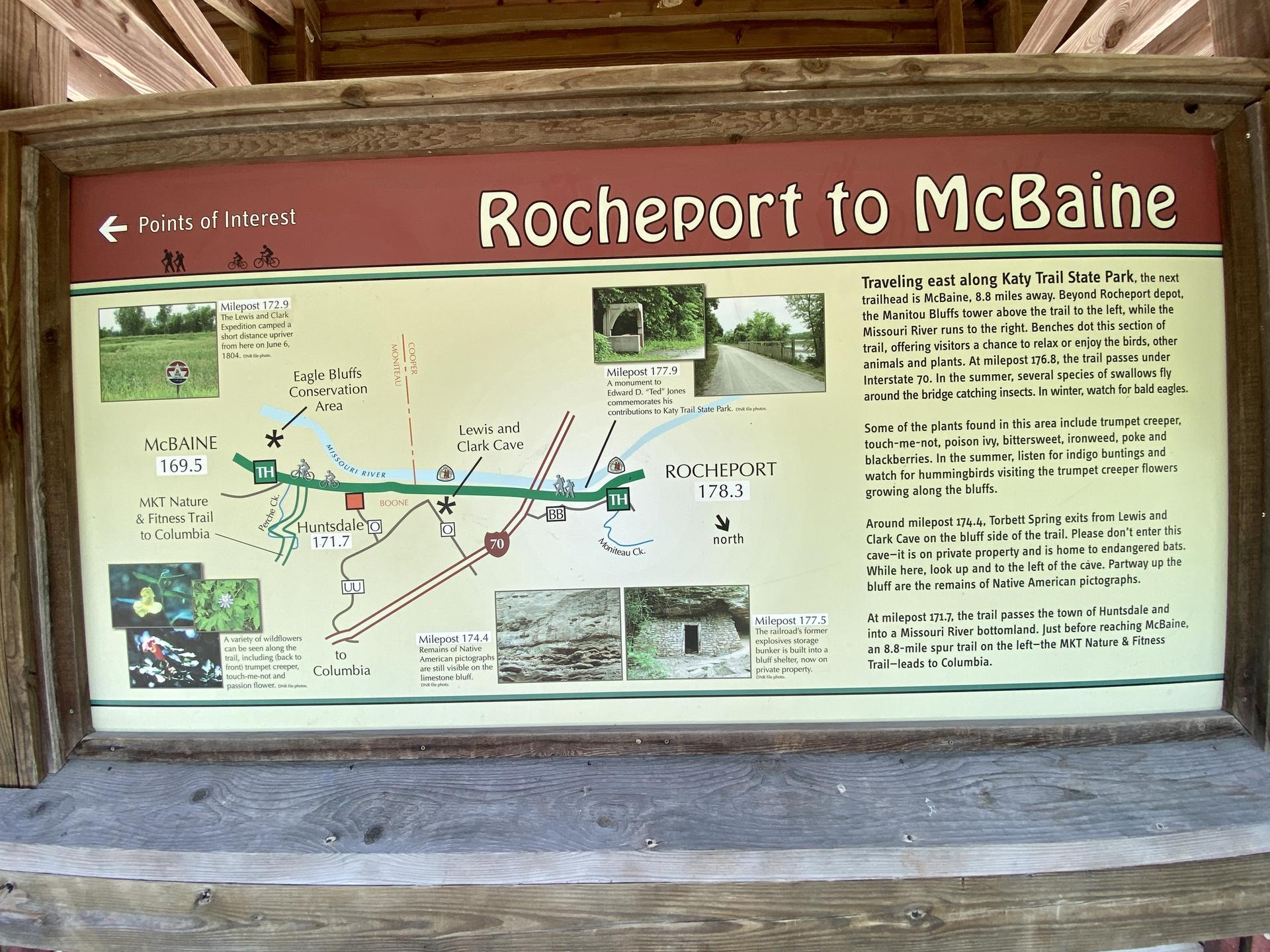 An outdoor information sign with a map and text under a wooden shelter.