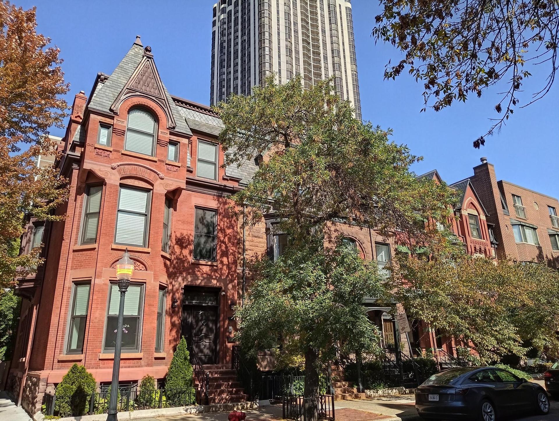 Historic red brick townhouses with autumn trees and a modern skyscraper behind.
