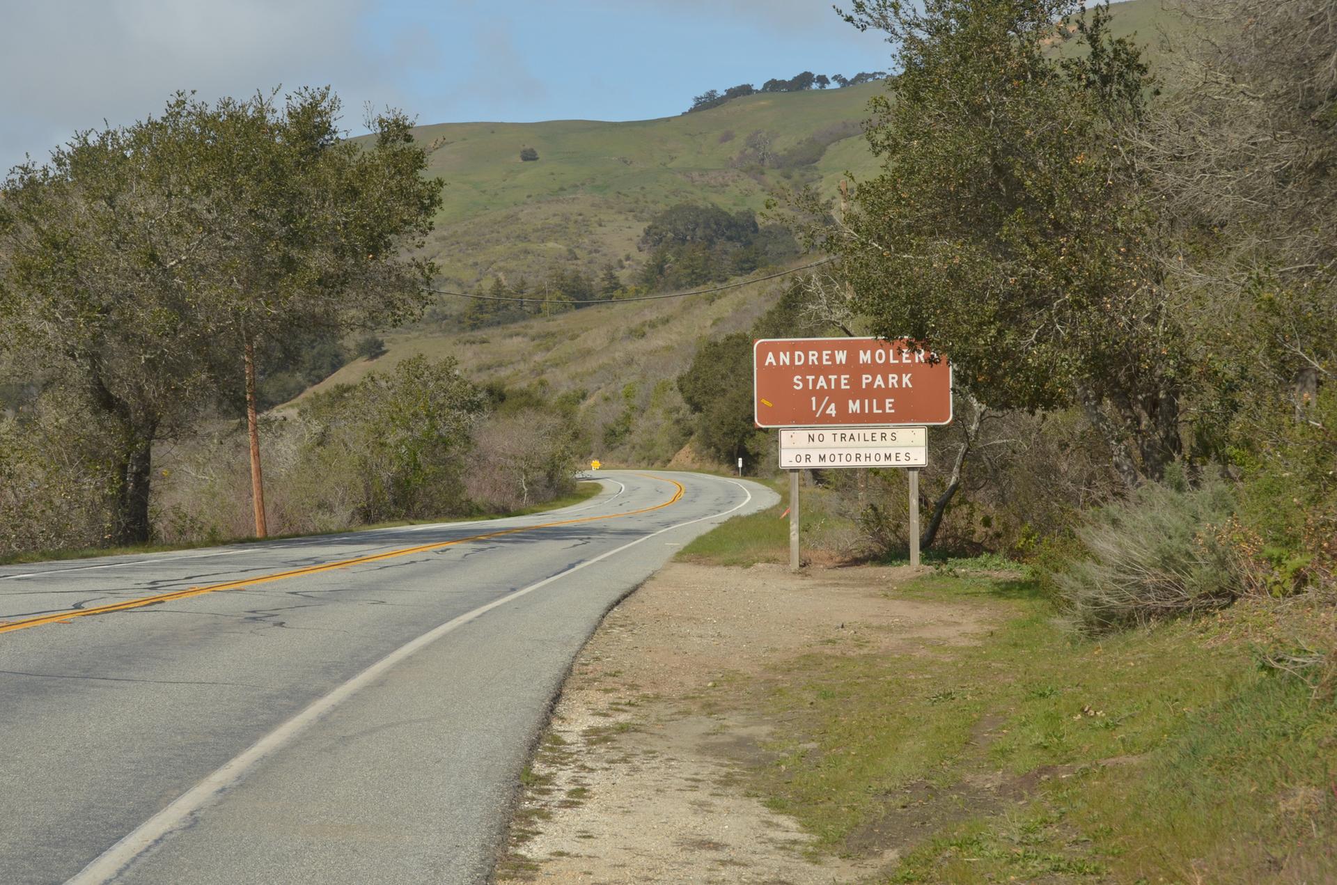 A winding road next to a brown sign, leading into green hills.