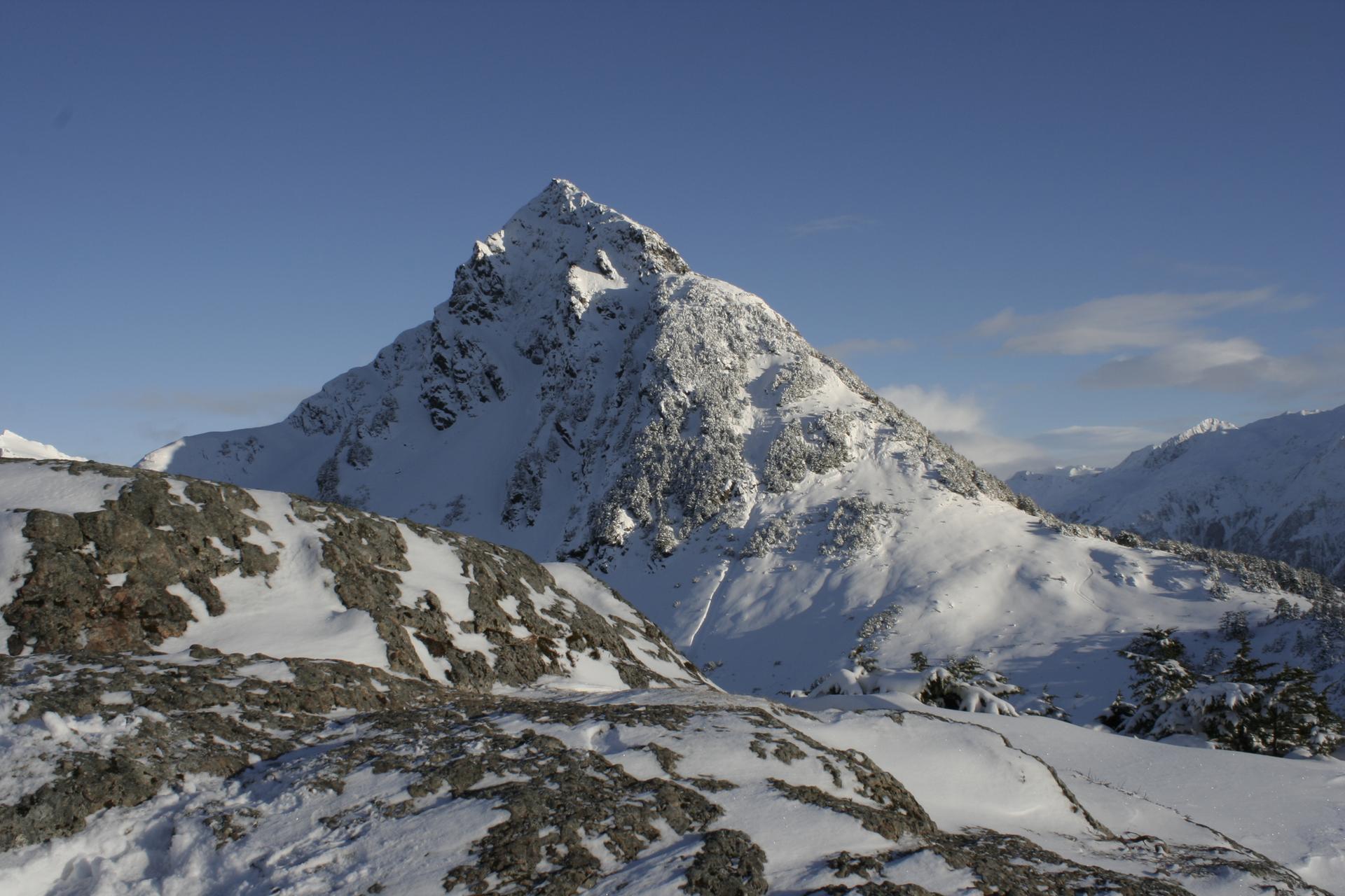 Majestic snow-covered mountain peak with rocky foreground under a clear blue sky.