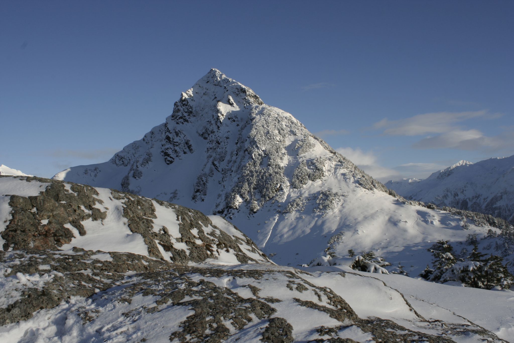 Majestic snow-covered mountain peak with rocky foreground under a clear blue sky. - Mount Verstovia Trail