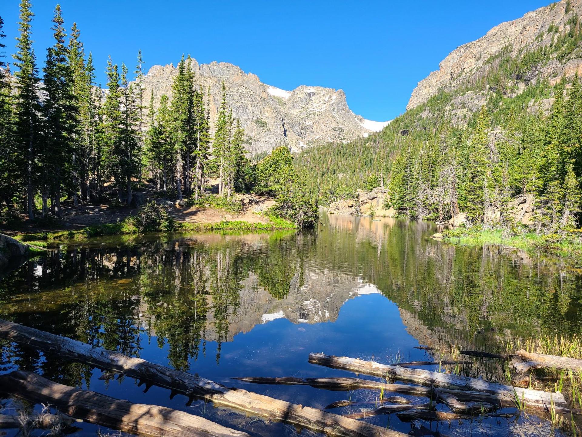 Serene mountain lake reflecting snow-capped peaks and blue sky, surrounded by pines.