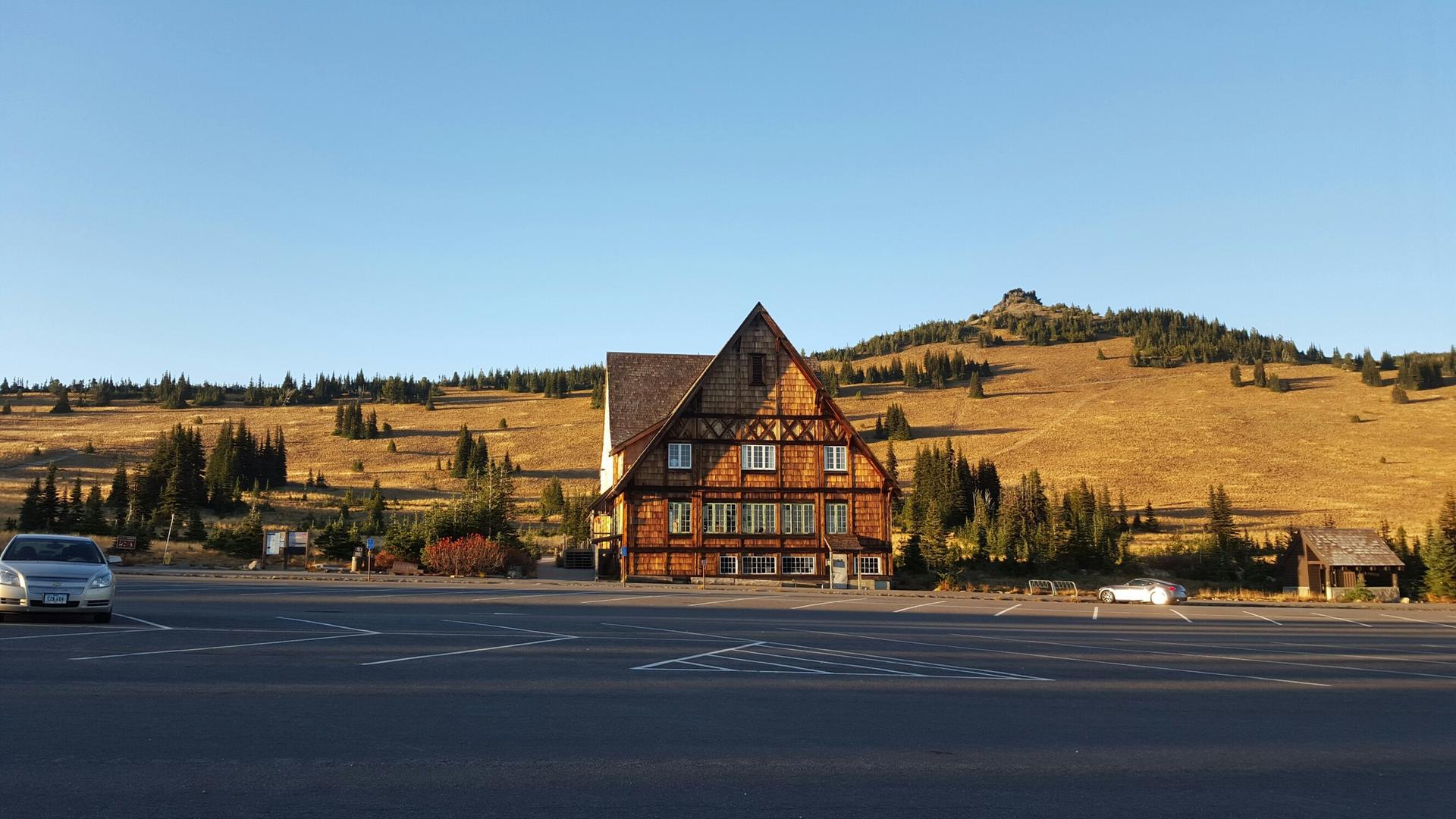 Large wooden building in an empty parking lot with golden hills behind it.