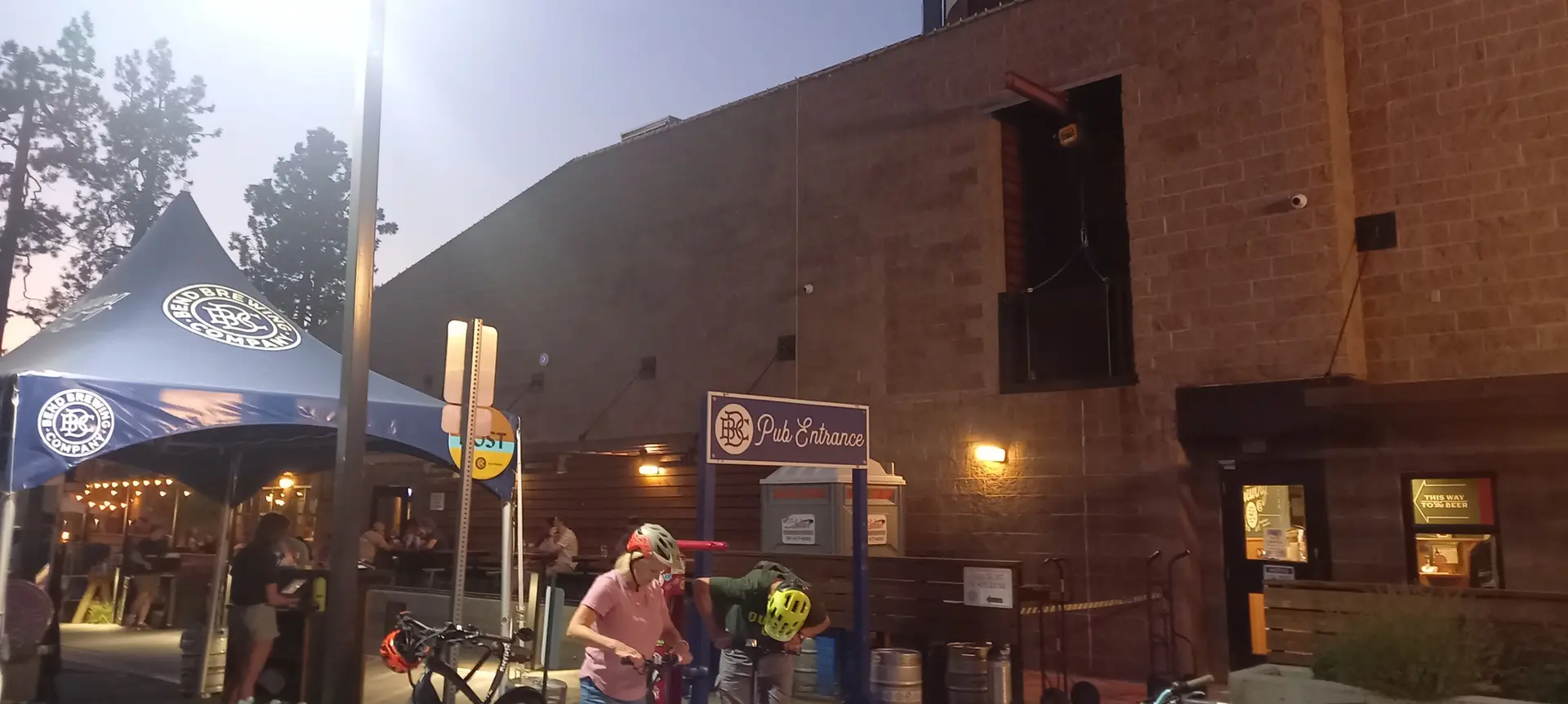 People with bikes gather outside a pub entrance at dusk.