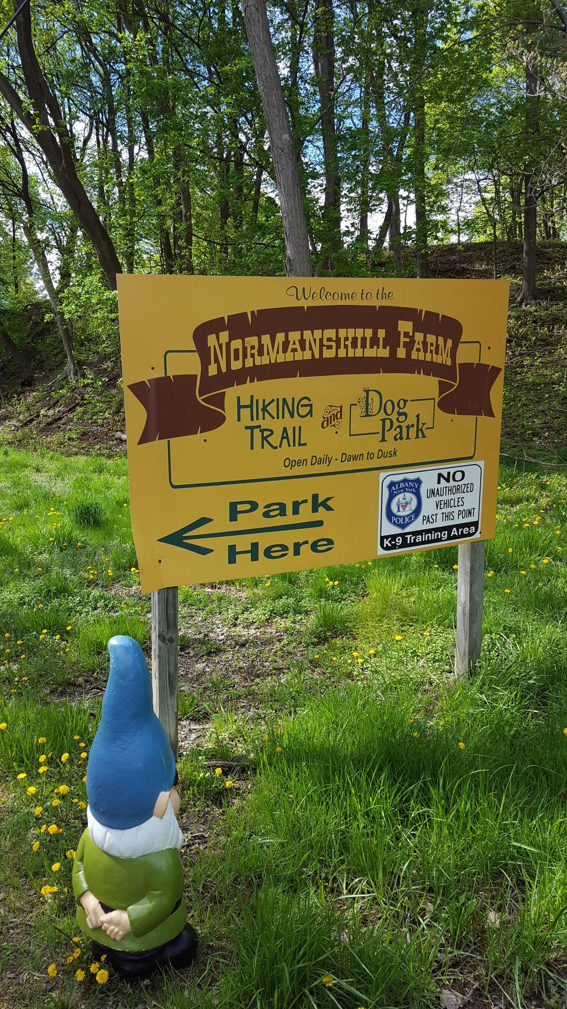 A yellow sign for a hiking trail and dog park, with a garden gnome.