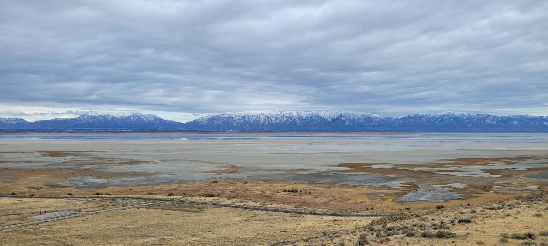 Vast flat landscape with distant snow-capped mountains under a cloudy sky.
