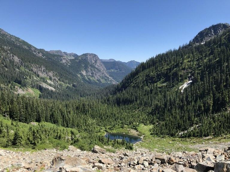 A small dark lake in a deep, forested mountain valley under a clear sky.