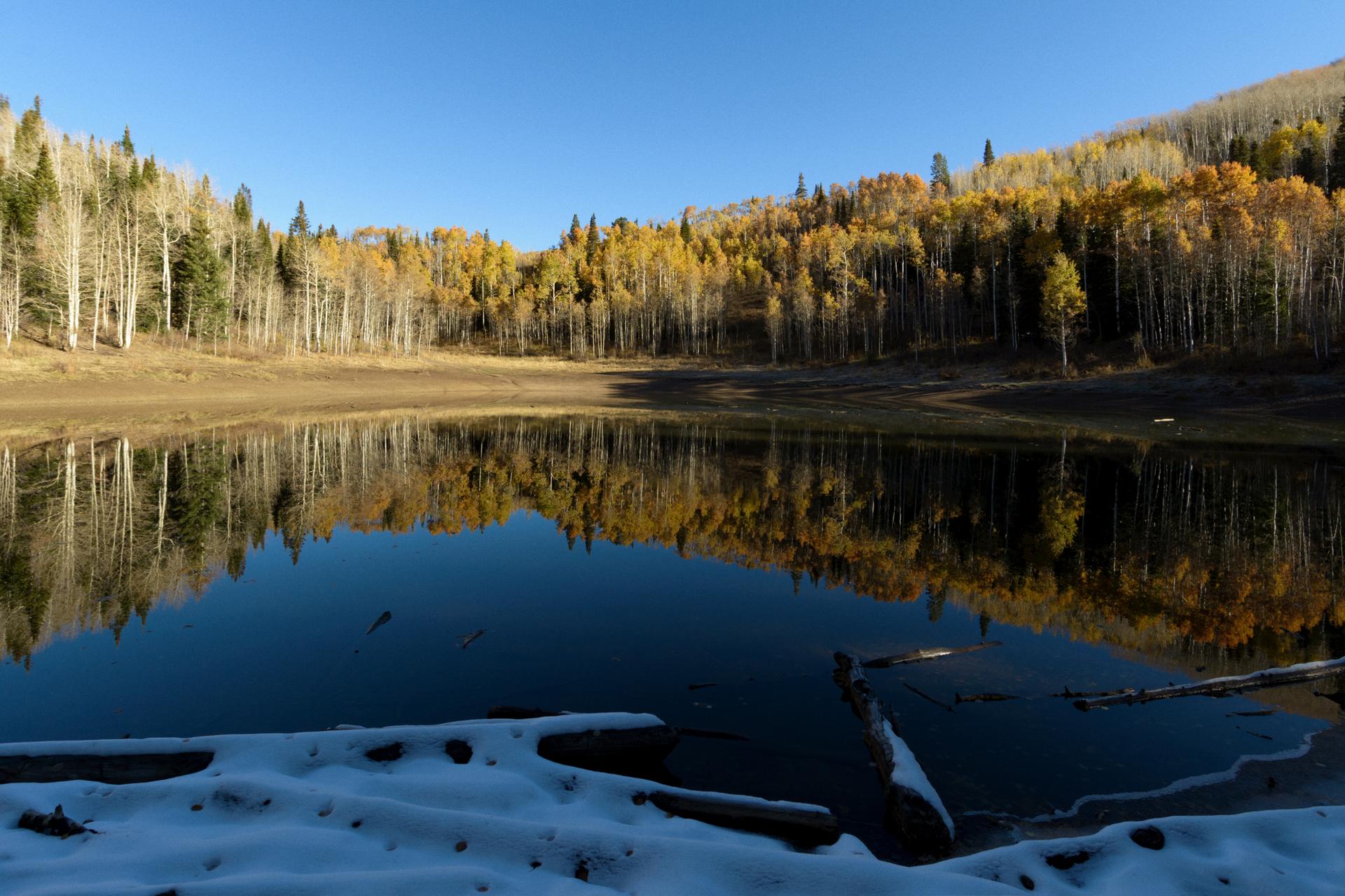 A calm lake reflects vibrant autumn trees under a clear blue sky.