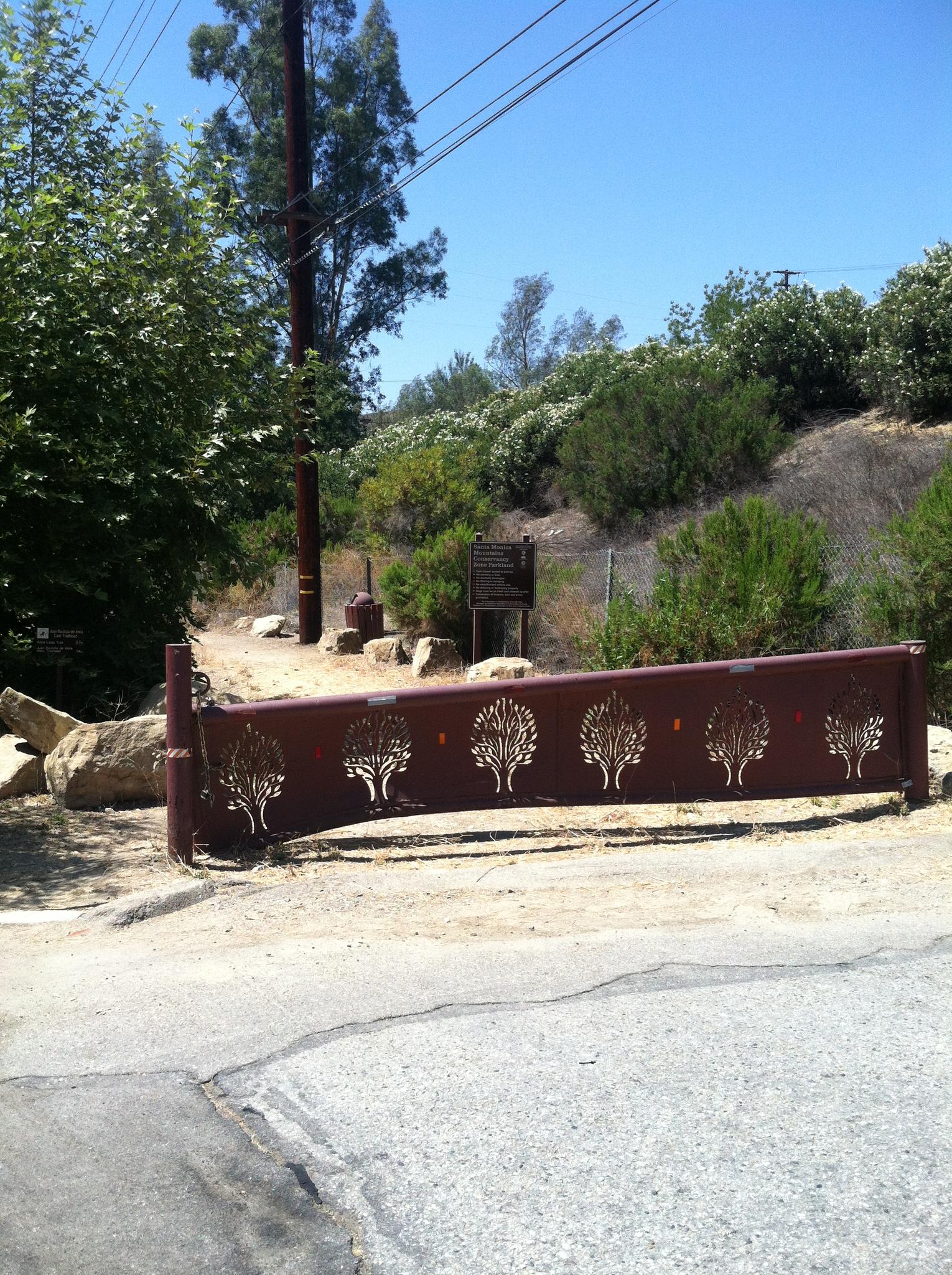 Brown metal gate with tree designs on a sunny dirt path.