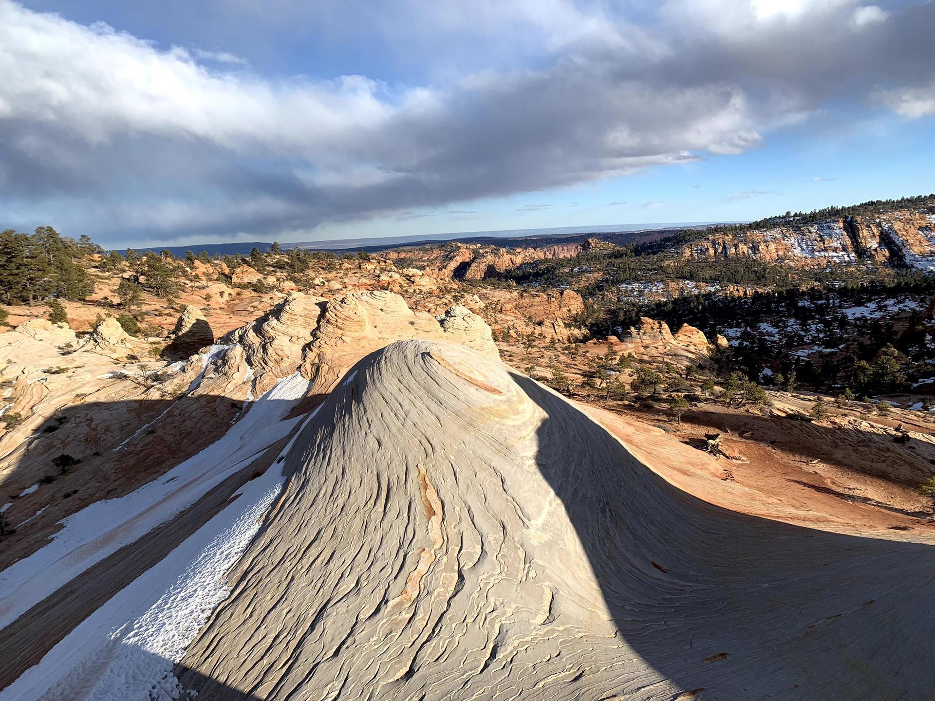 Wavy rock formation with patches of snow, overlooking a vast desert landscape.