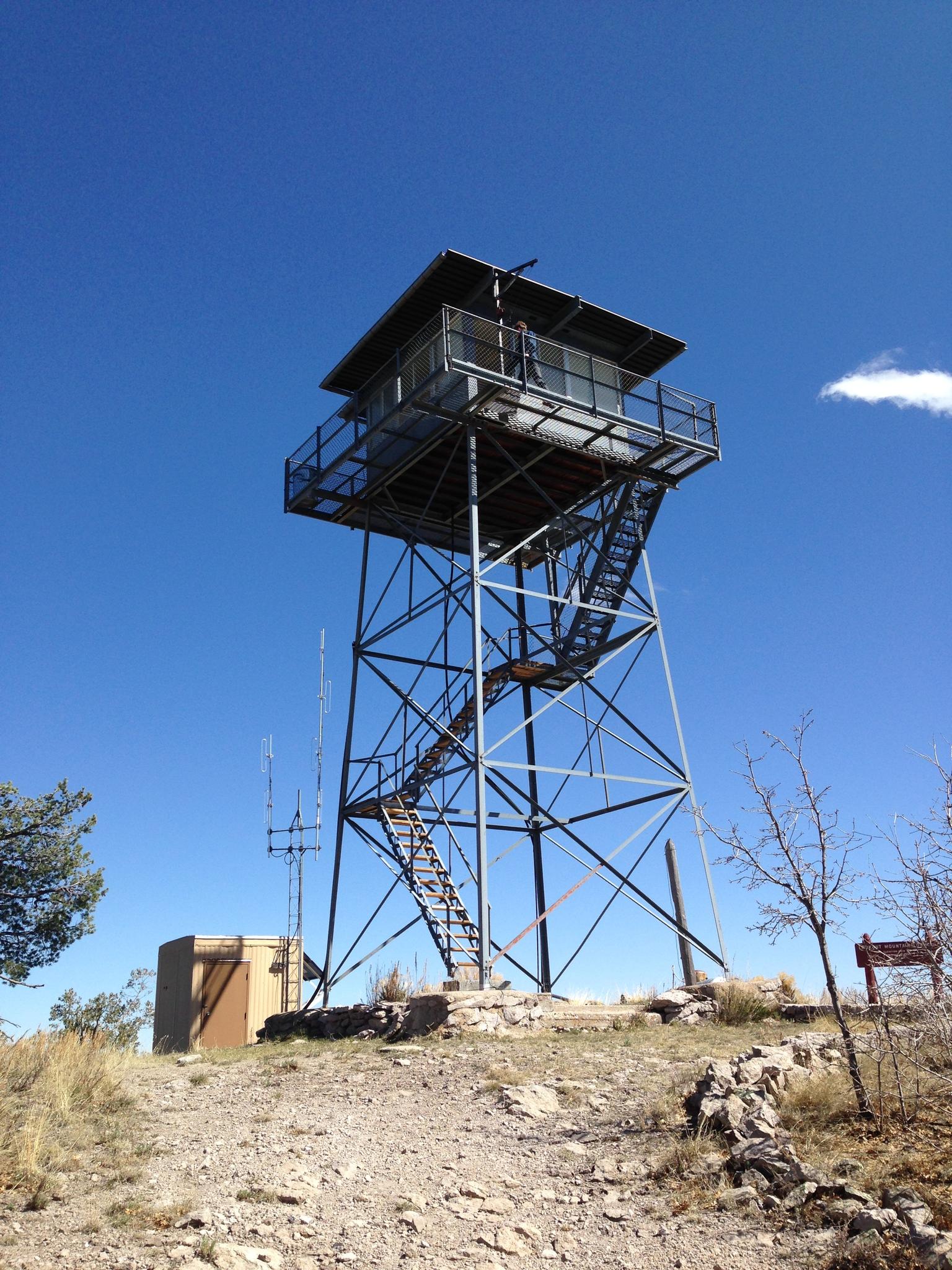 Metal fire lookout tower on a rocky hill under a bright blue sky.