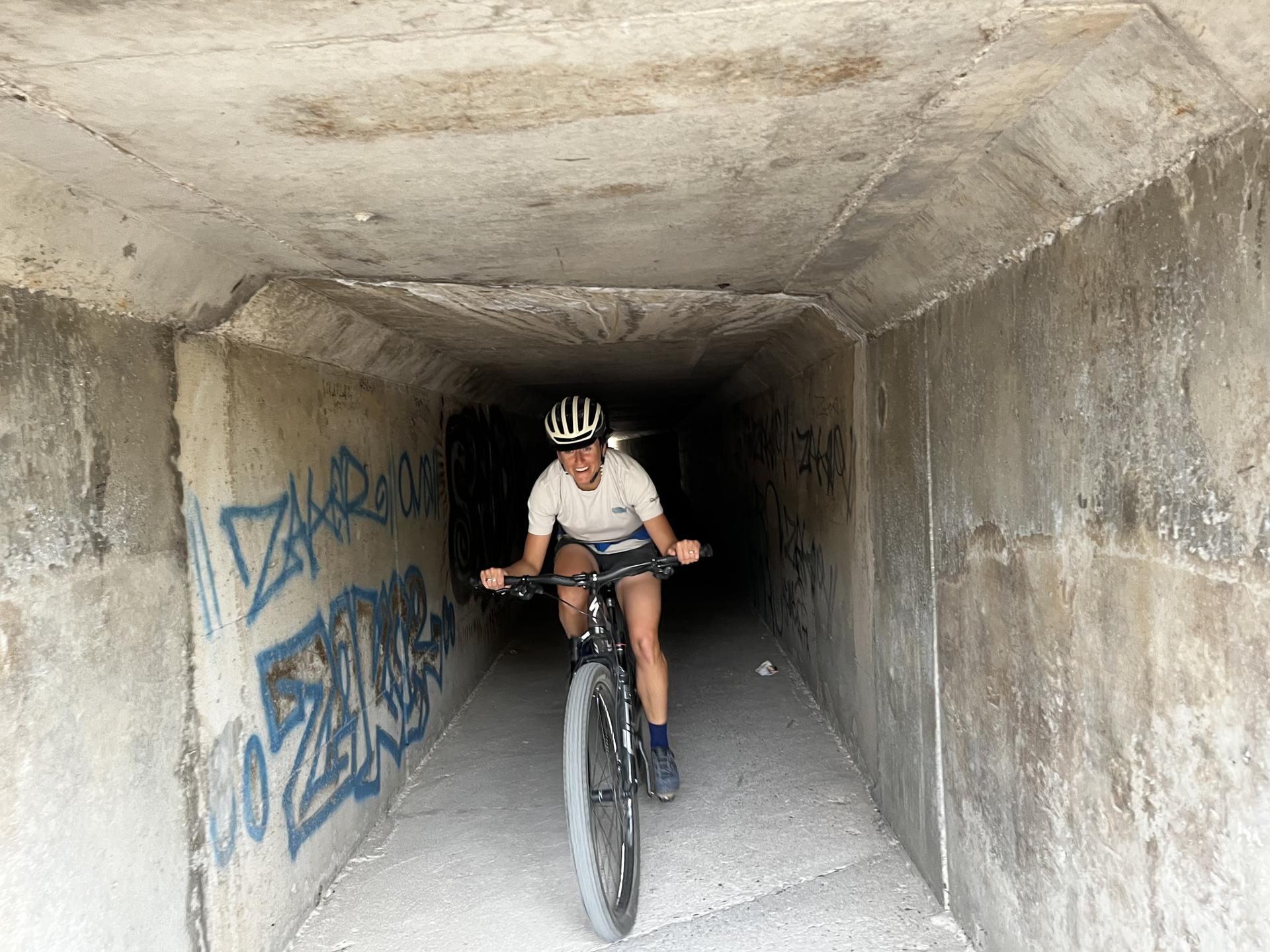 Cyclist wearing a helmet rides a mountain bike through a concrete tunnel.