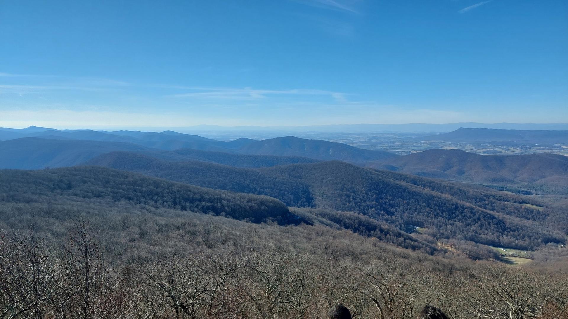 Expansive view of bare forested mountains and distant valley under a clear blue sky.