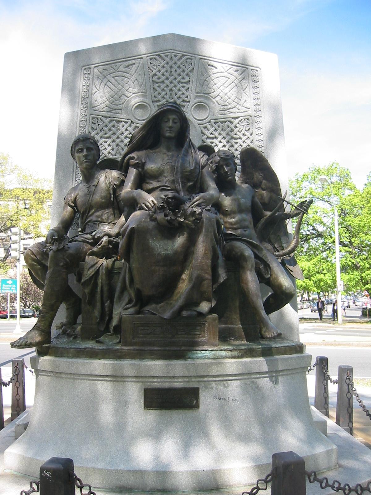 Ornate bronze statue of figures on a stone base under bright daylight.