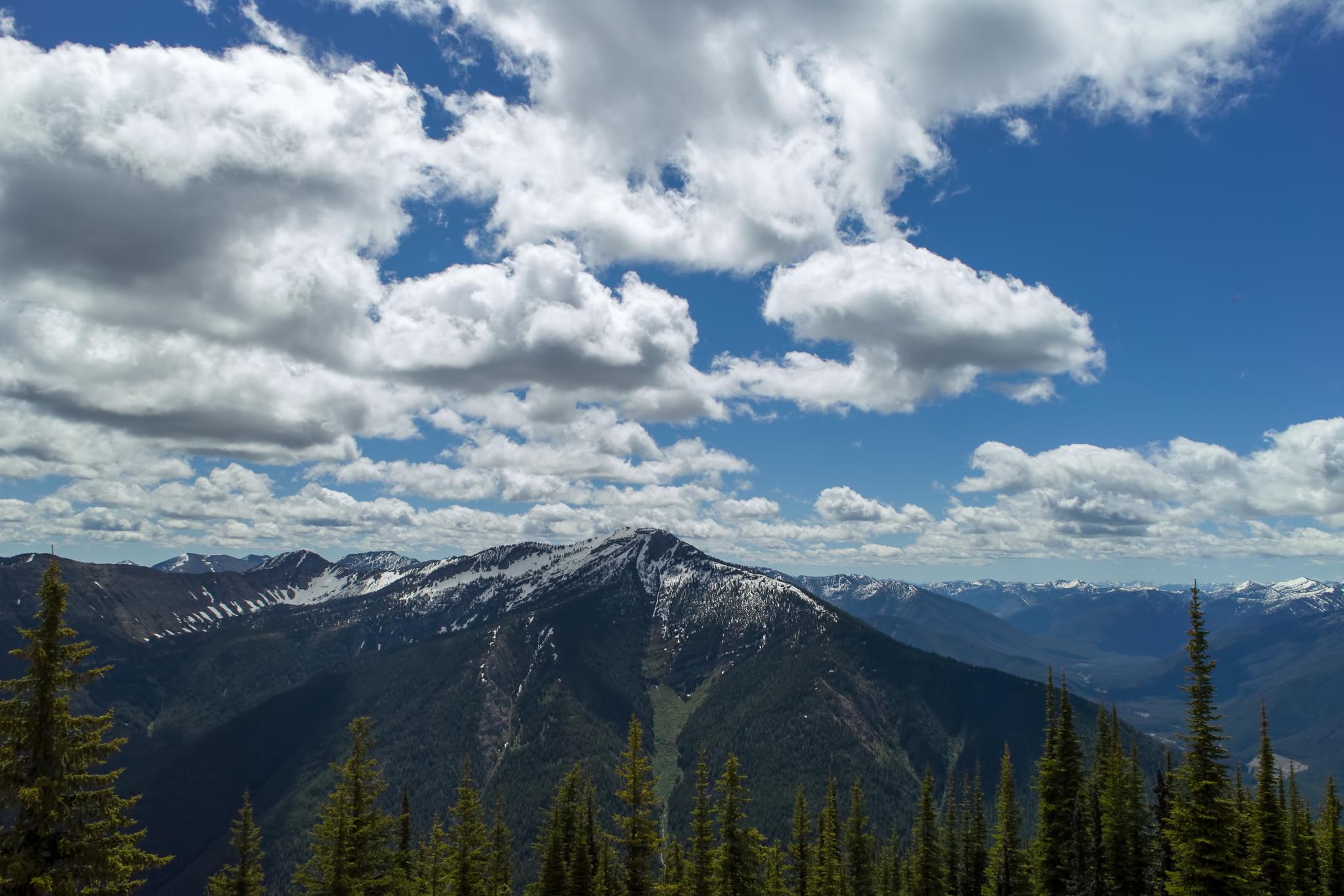 Vast mountain range with snow-capped peaks under a bright, cloudy blue sky.
