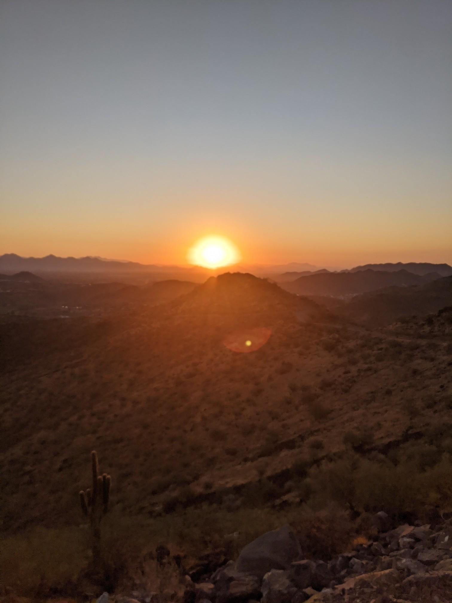 Golden sunset over desert mountains with a saguaro cactus in the foreground.