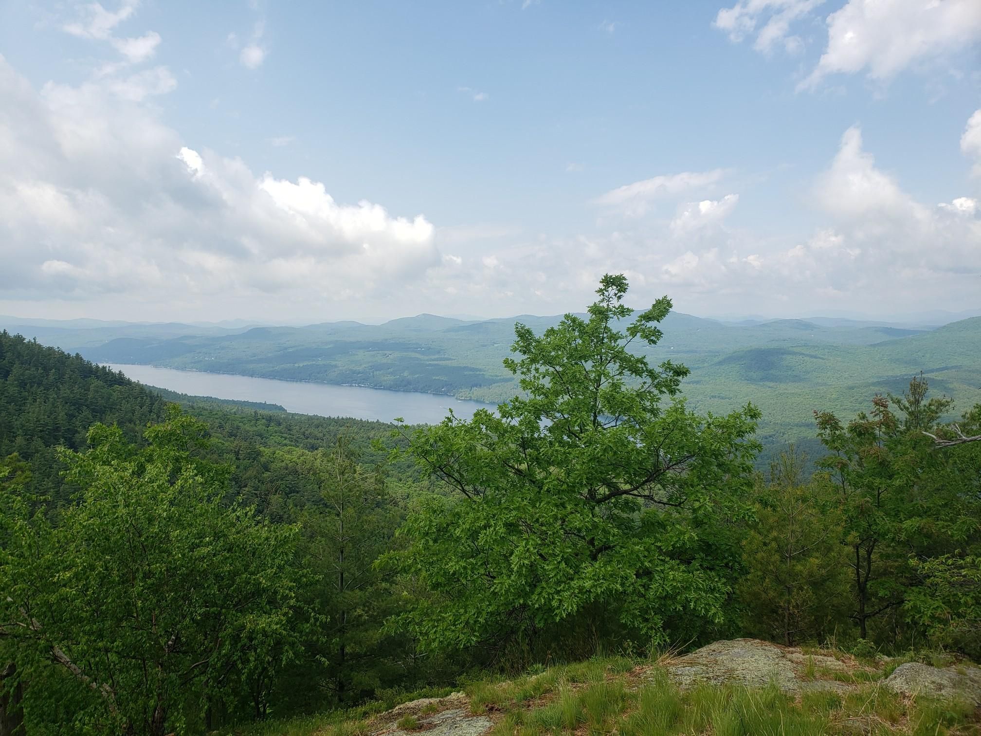 Elevated view of a large lake surrounded by green forested mountains under cloudy skies. - Tongue Mountain Range Loop