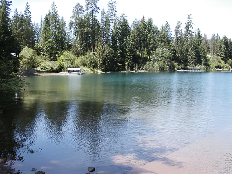 Clear lake with forested shore, a covered boat docked, under bright daylight.