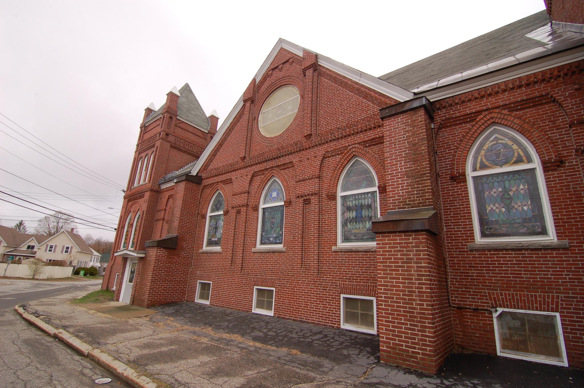 Red brick church with stained glass windows on an overcast day.
