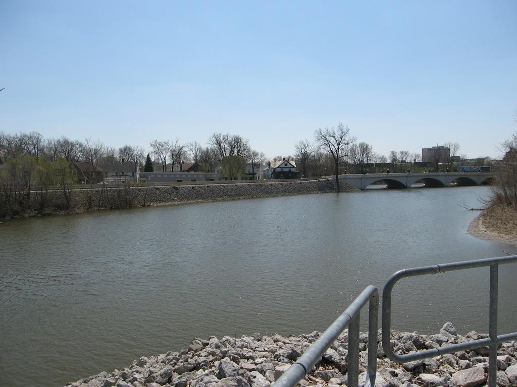 A wide river with a stone bridge and trees under a bright blue sky.