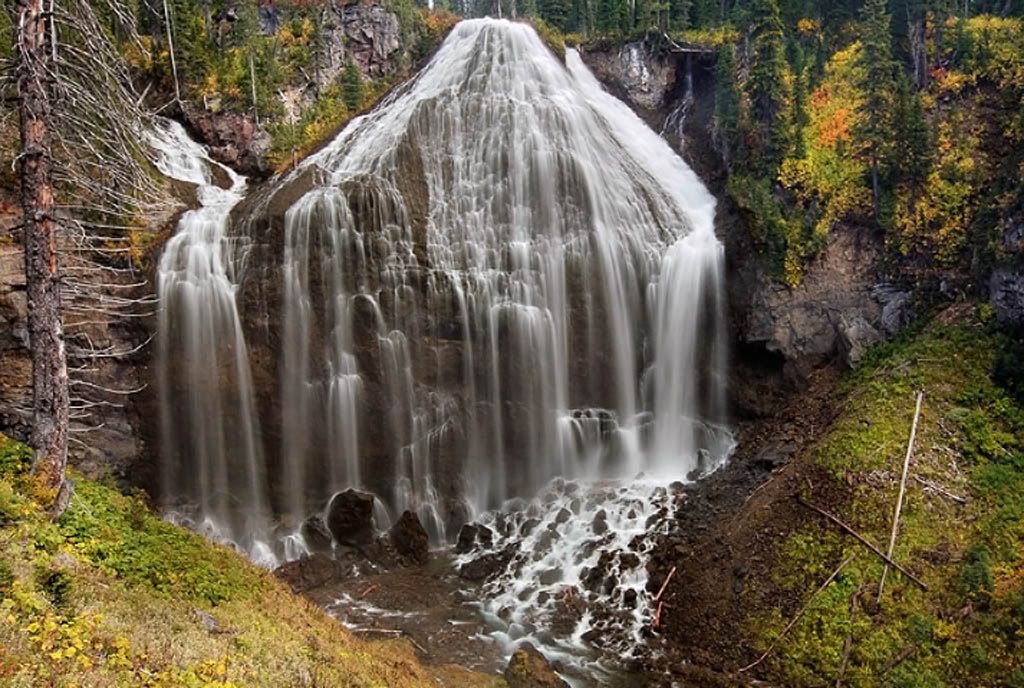 A wide, multi-stream waterfall flows over rocky cliffs in a forest. - Union Falls Trail