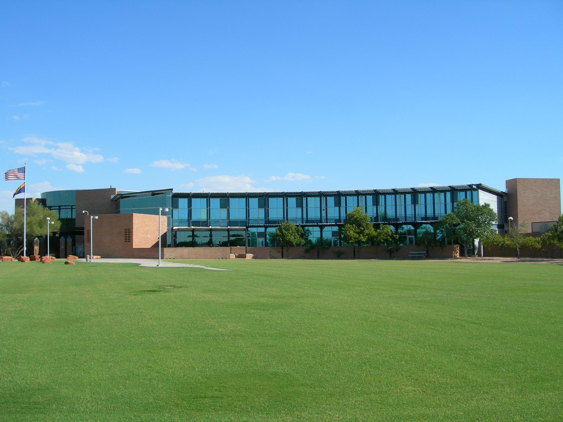 A modern building with a glass facade overlooks a wide green lawn.