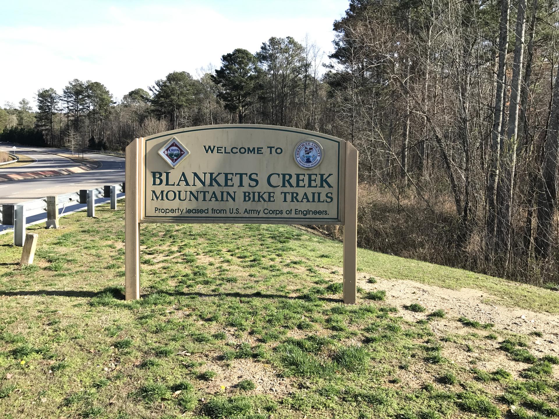 A wooden welcome sign for mountain bike trails on a sunny day.