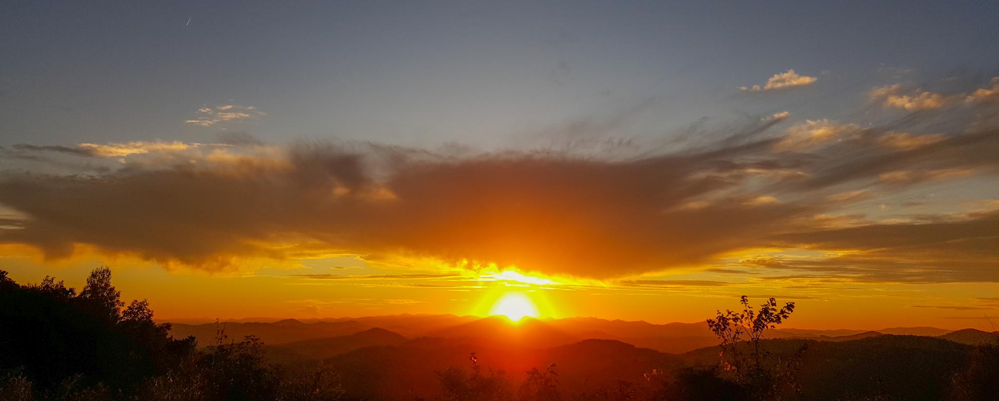 A vibrant orange and yellow sunset over distant mountain ranges.