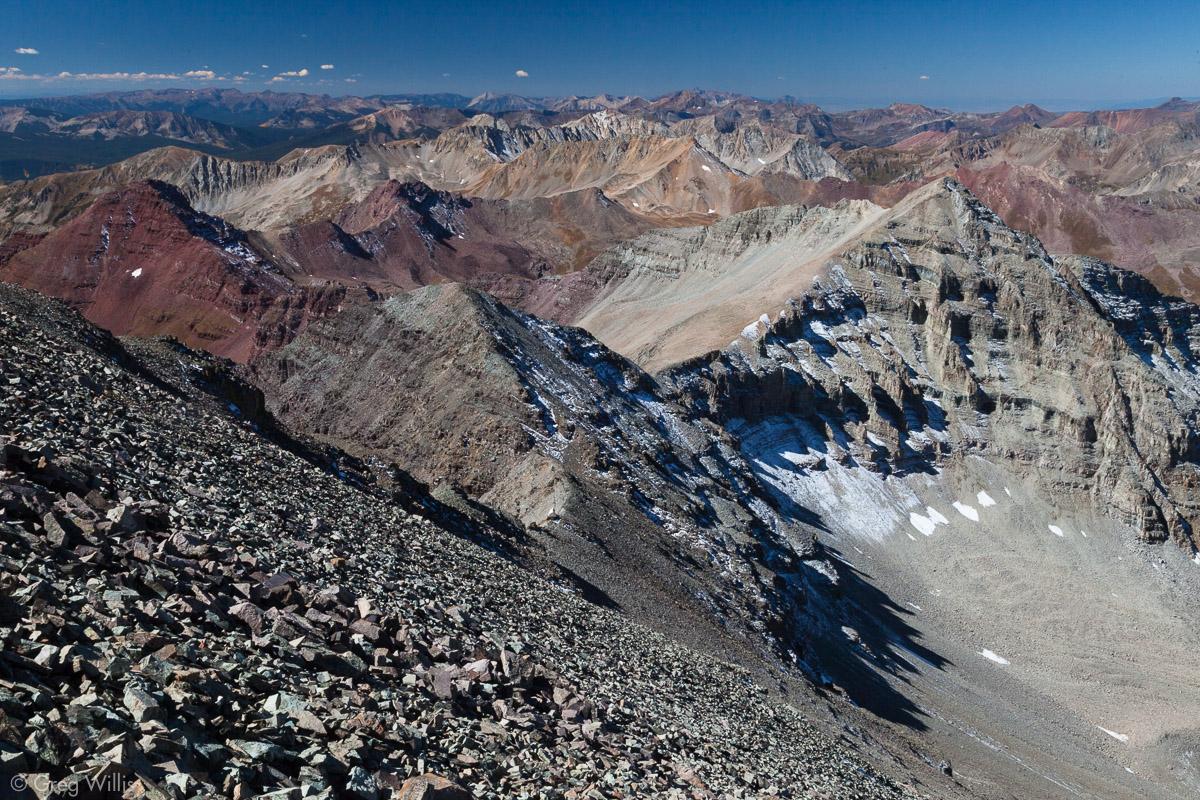 Vast mountain range with colorful peaks, scree slope, and a tiny hiker.