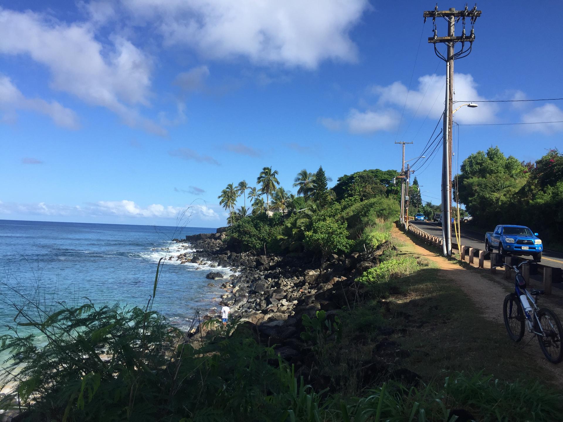 Coastal road with utility poles, rocky shore, ocean, and a parked bicycle.