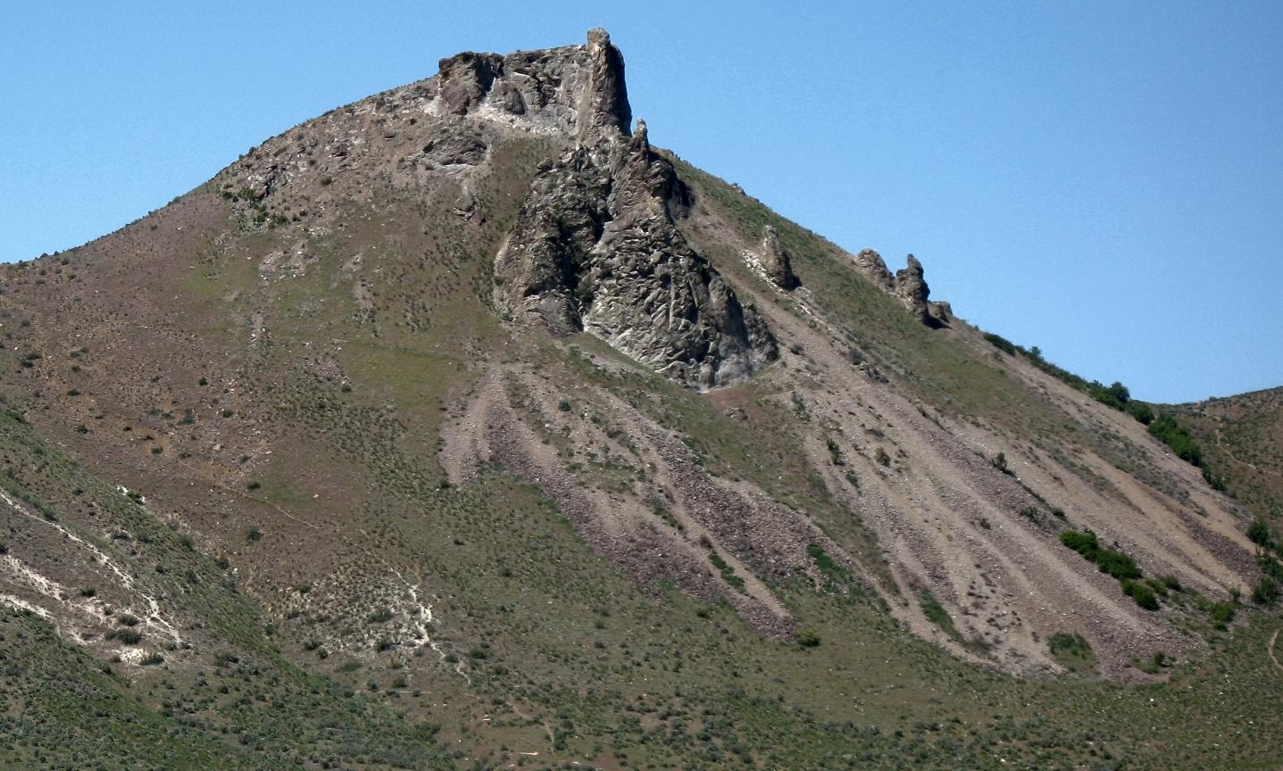 A rugged mountain peak with rocky outcrops and dry grassy slopes under clear sky.