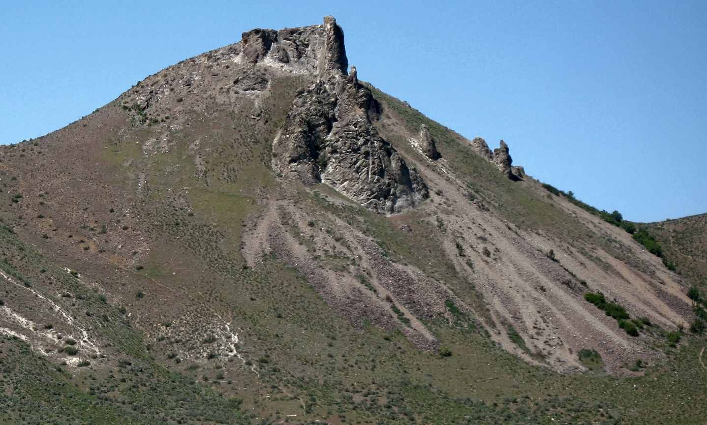 A rugged mountain peak with rocky outcrops and dry grassy slopes under clear sky. - Castle Rock Trail