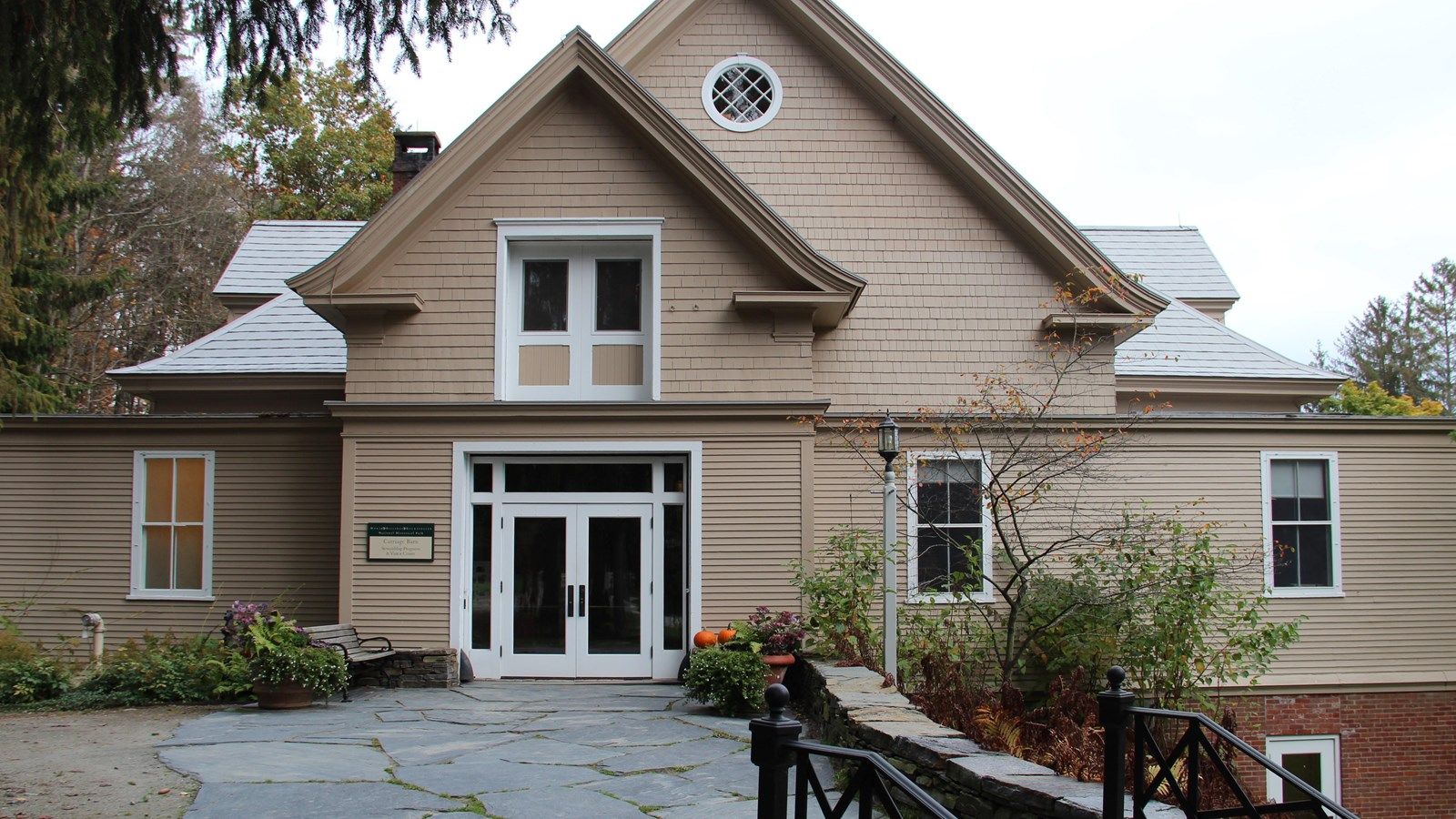 Large beige building with white trim and a stone path on an overcast day. - Carriage Barn Visitor Center – Woodstock Middle Covered Bridge loop from Lincoln Covered Bridge