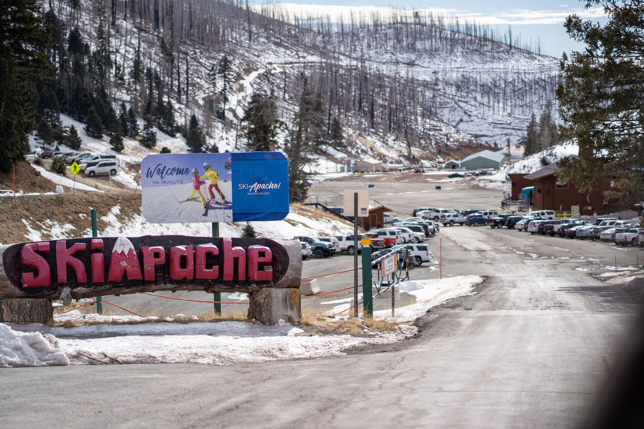 A large wooden sign and billboard at a snowy mountain resort entrance with parked cars. - Lookout Mountain via Crest and Scenic Trails