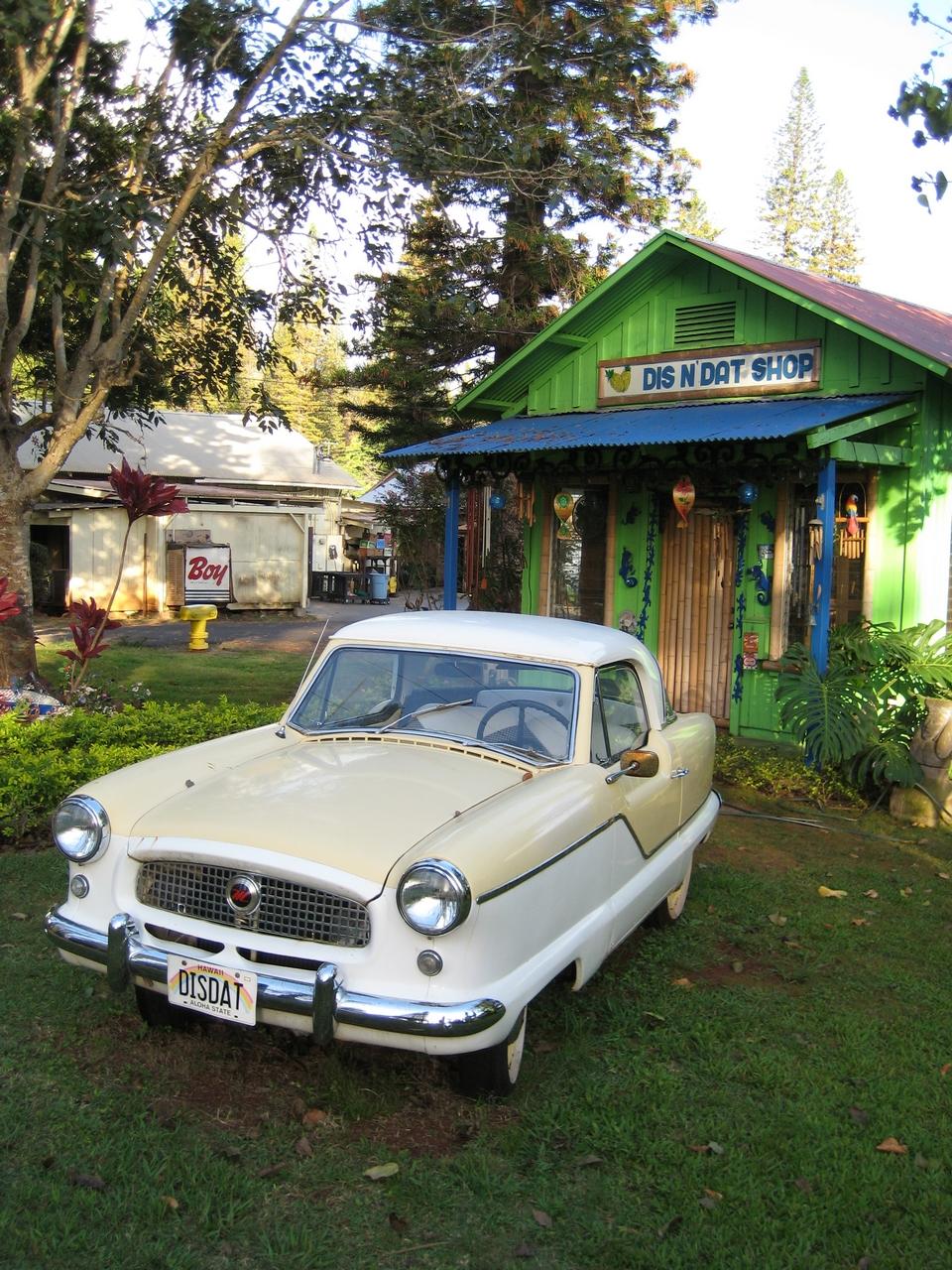 A vintage cream and white car parked on grass near a bright green shop.
