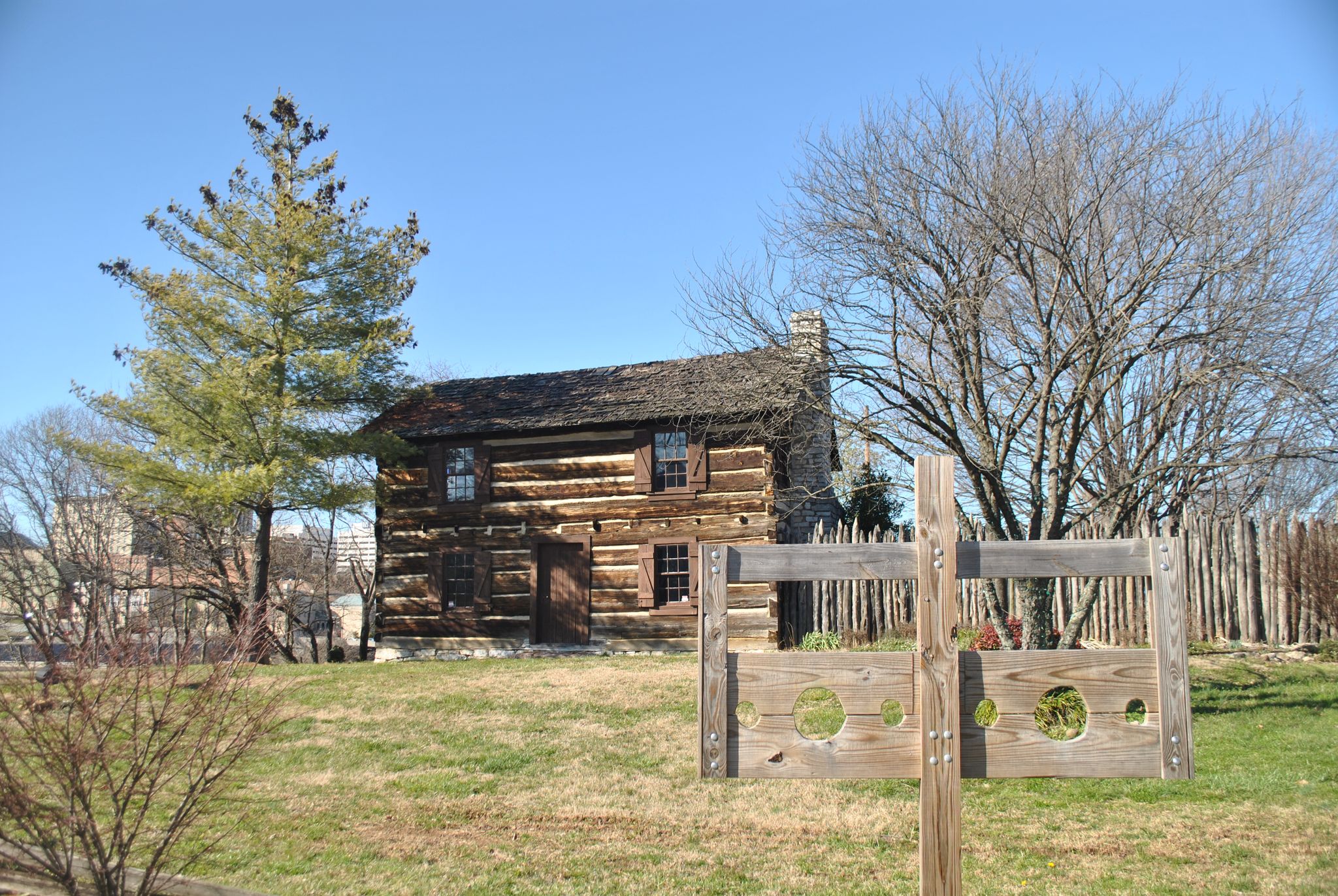 Historic log cabin next to wooden stocks in a sunny, grassy field. - James White Fort – Neyland Greenway terminus loop from Knoxville