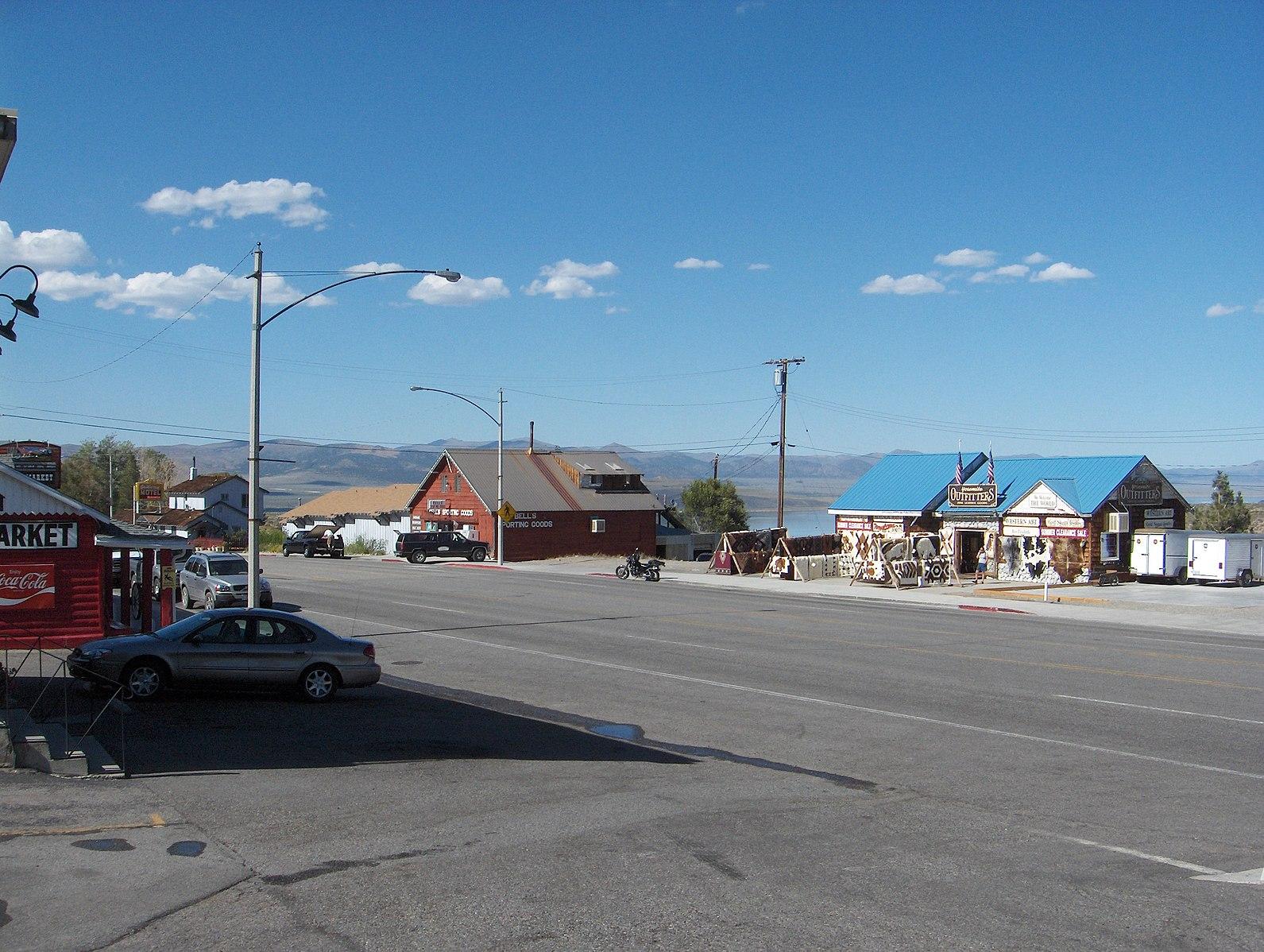 Bright daylight illuminates a street with buildings, parked cars, and distant hills.