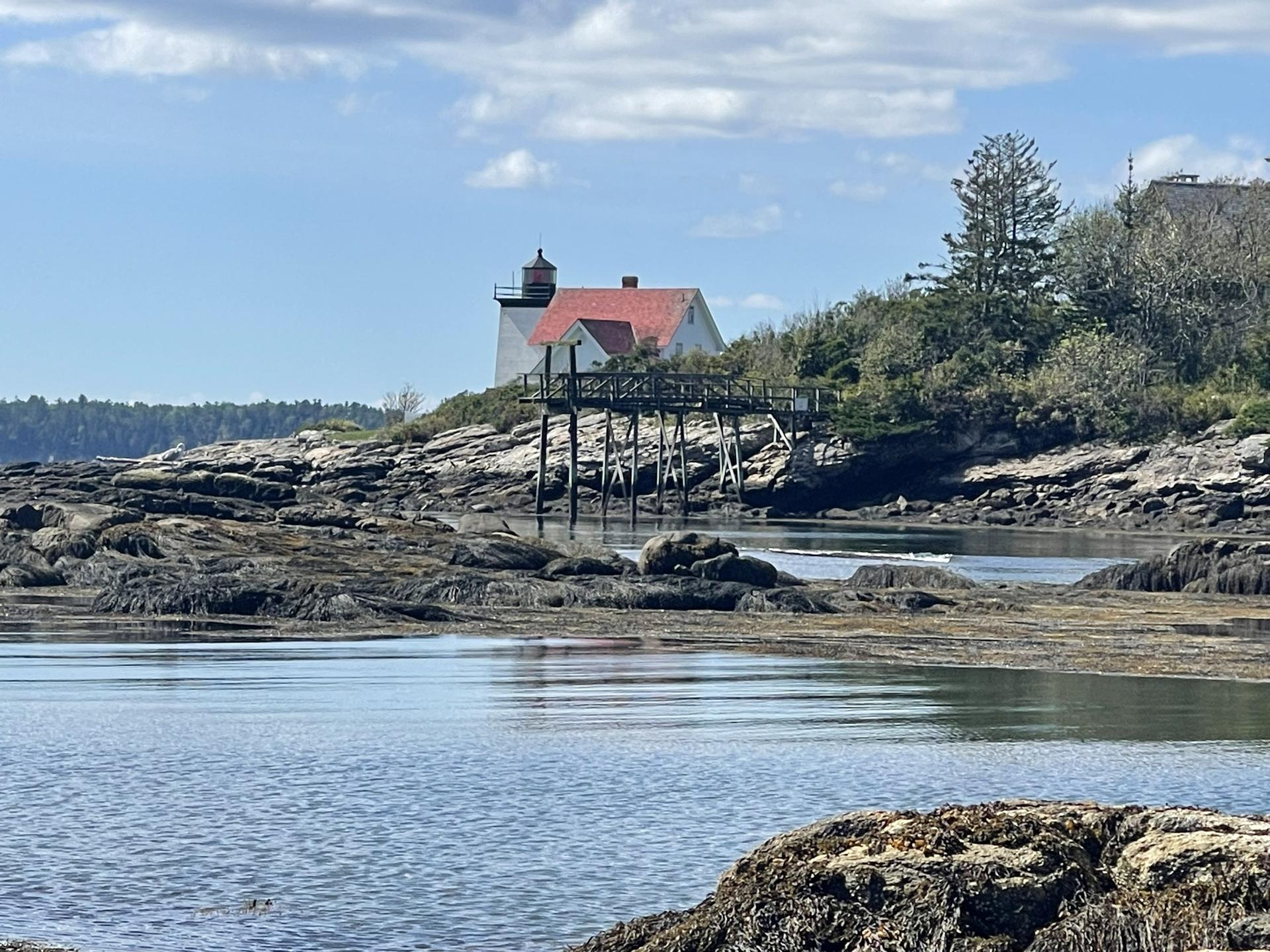 Lighthouse on a rocky island with a long wooden walkway over calm water.