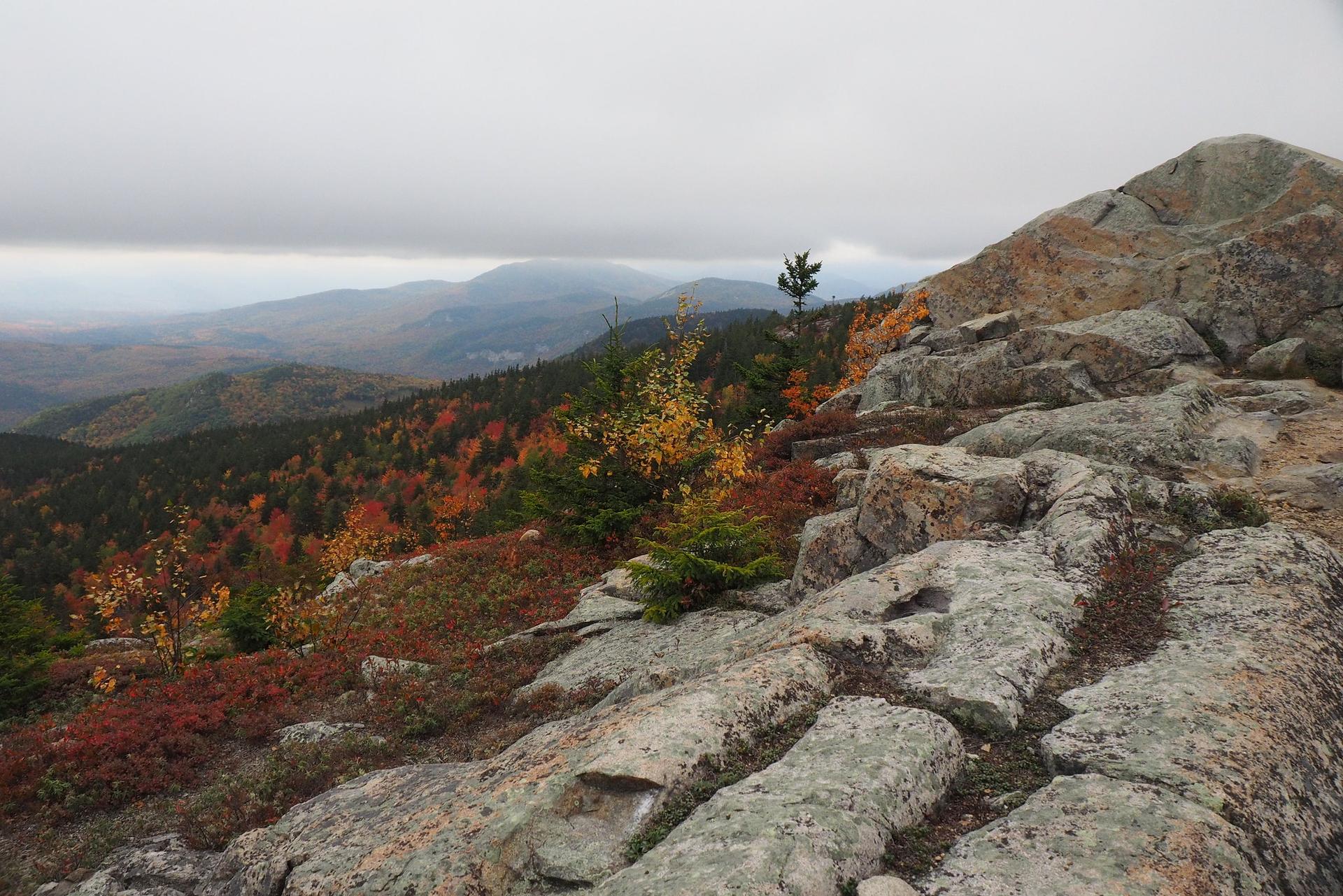 Rocky mountain peak with vibrant autumn foliage under an overcast sky.