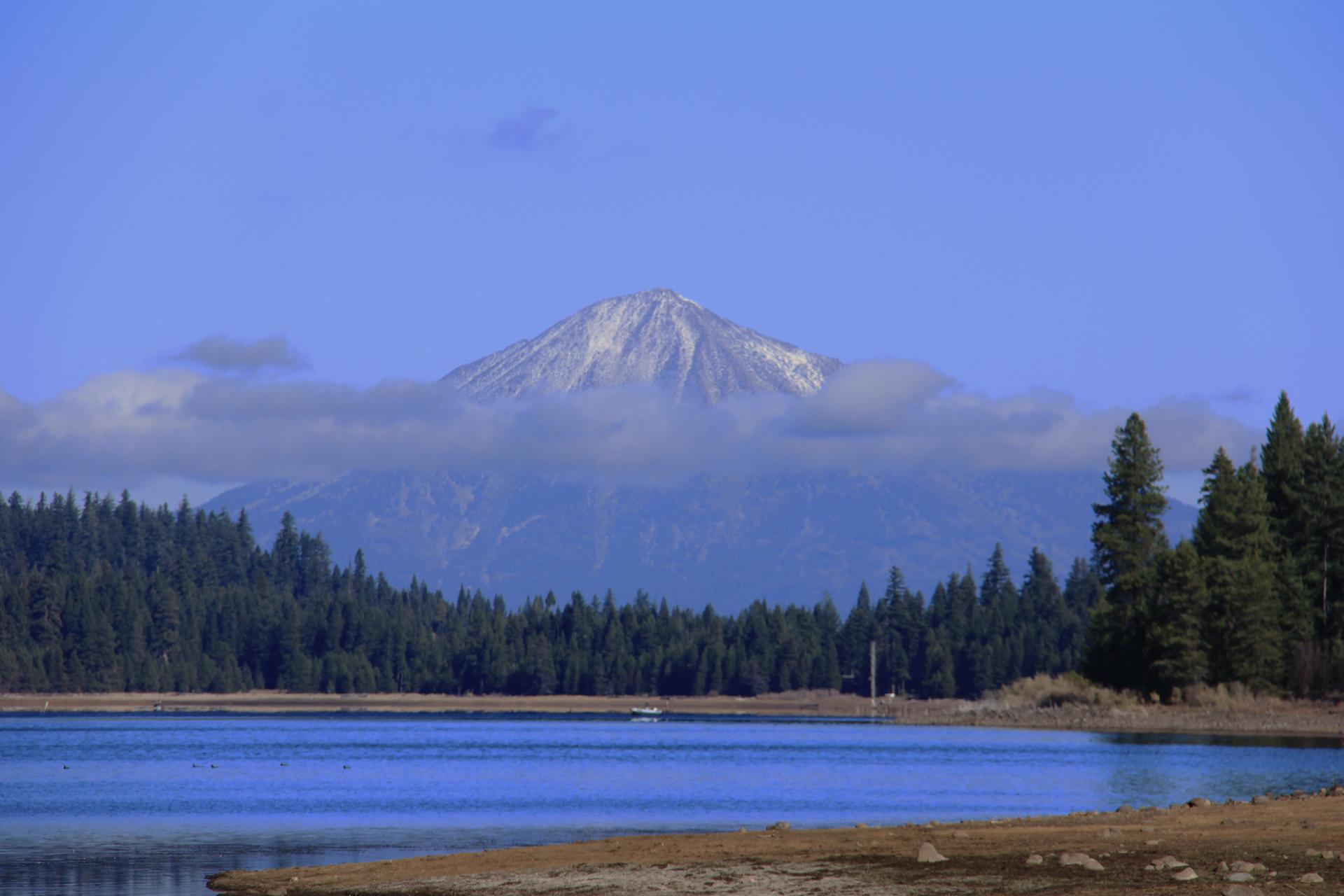Snow-capped mountain peak behind a lake and dark green forest.