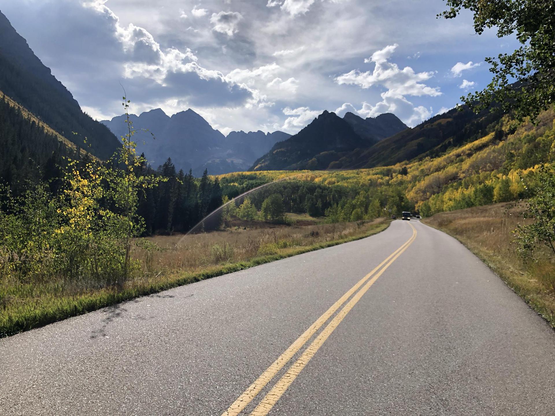 A winding road through a mountain valley with autumn trees under a cloudy sky.