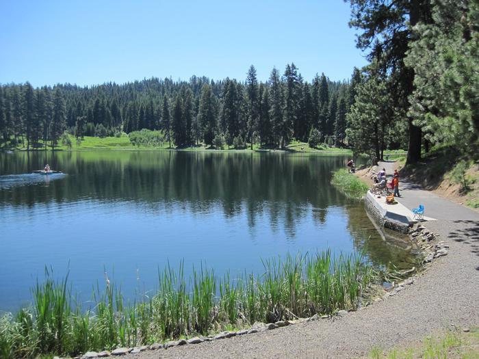 Sunny lake with people fishing from a dock and kayaking on the water.