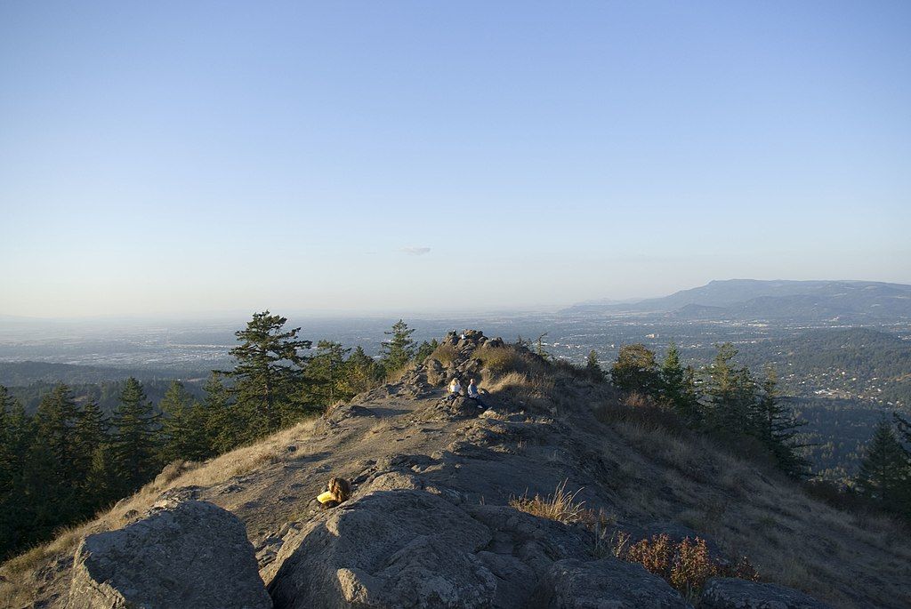 People gather on a rocky mountain ridge overlooking a distant city at sunset. - Spencer Butte via Ridgeline Trail