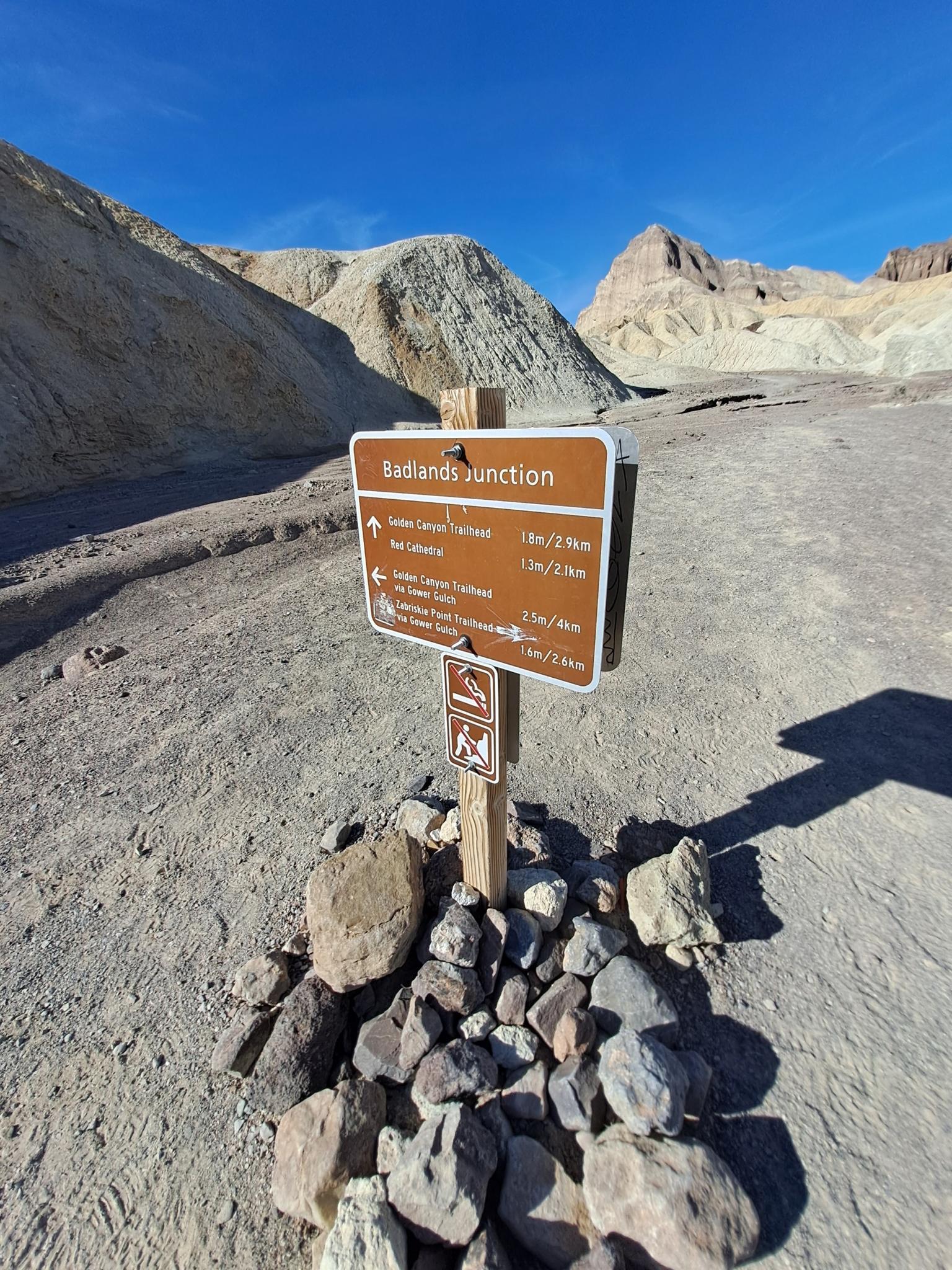 Brown trail sign on a rocky base in a desert landscape.