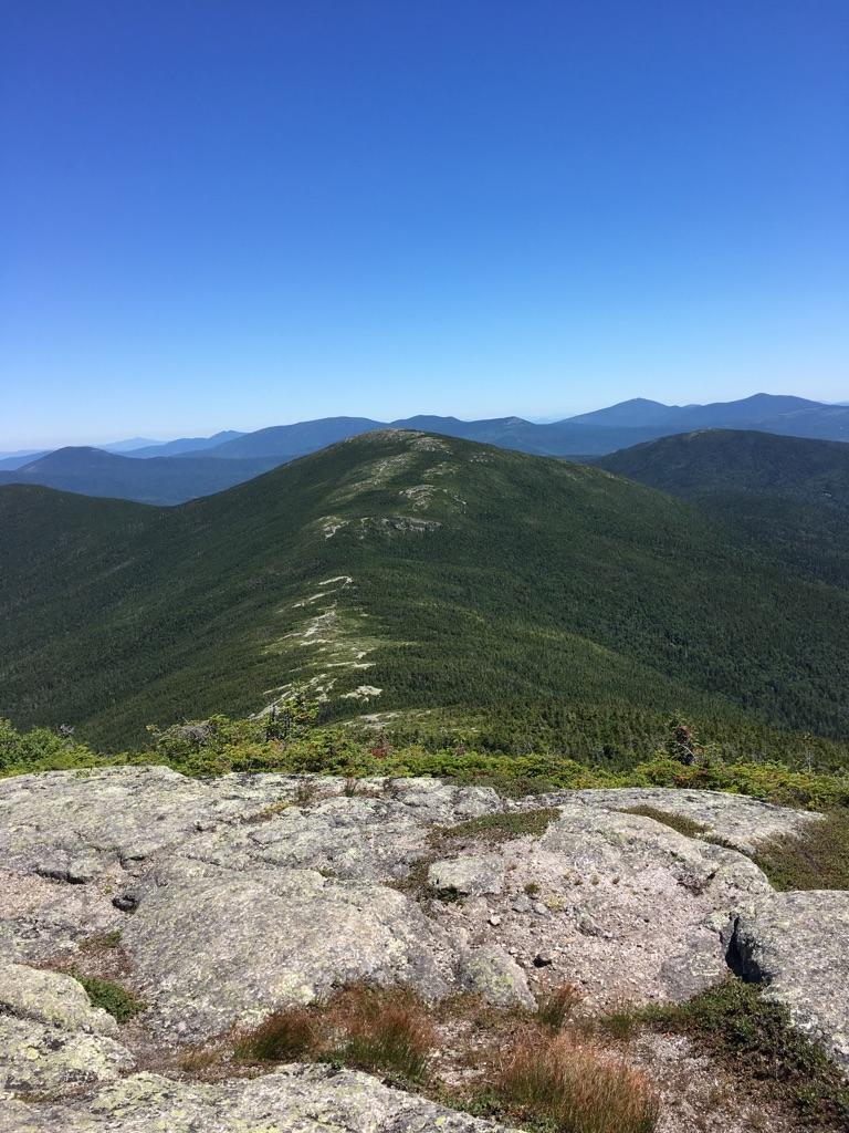 Sunny mountain view with rocky foreground and a winding ridge path.