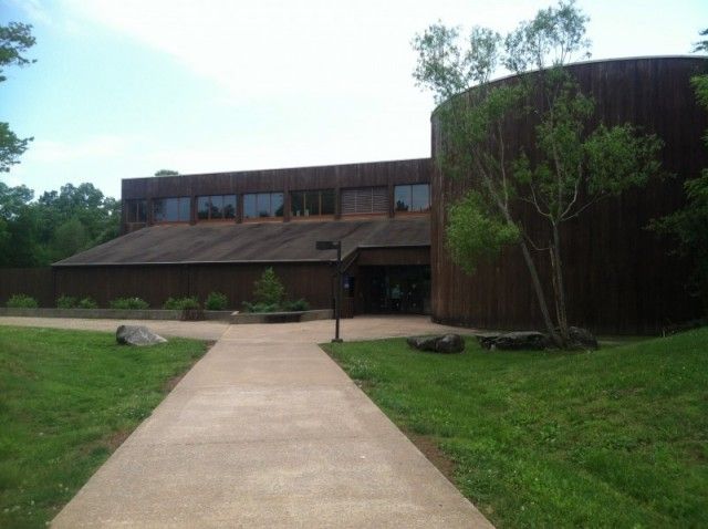 A large wooden building with a concrete path on a bright day. - Golden Pond Visitor Center – Elk & Bison Prairie loop from Fenton