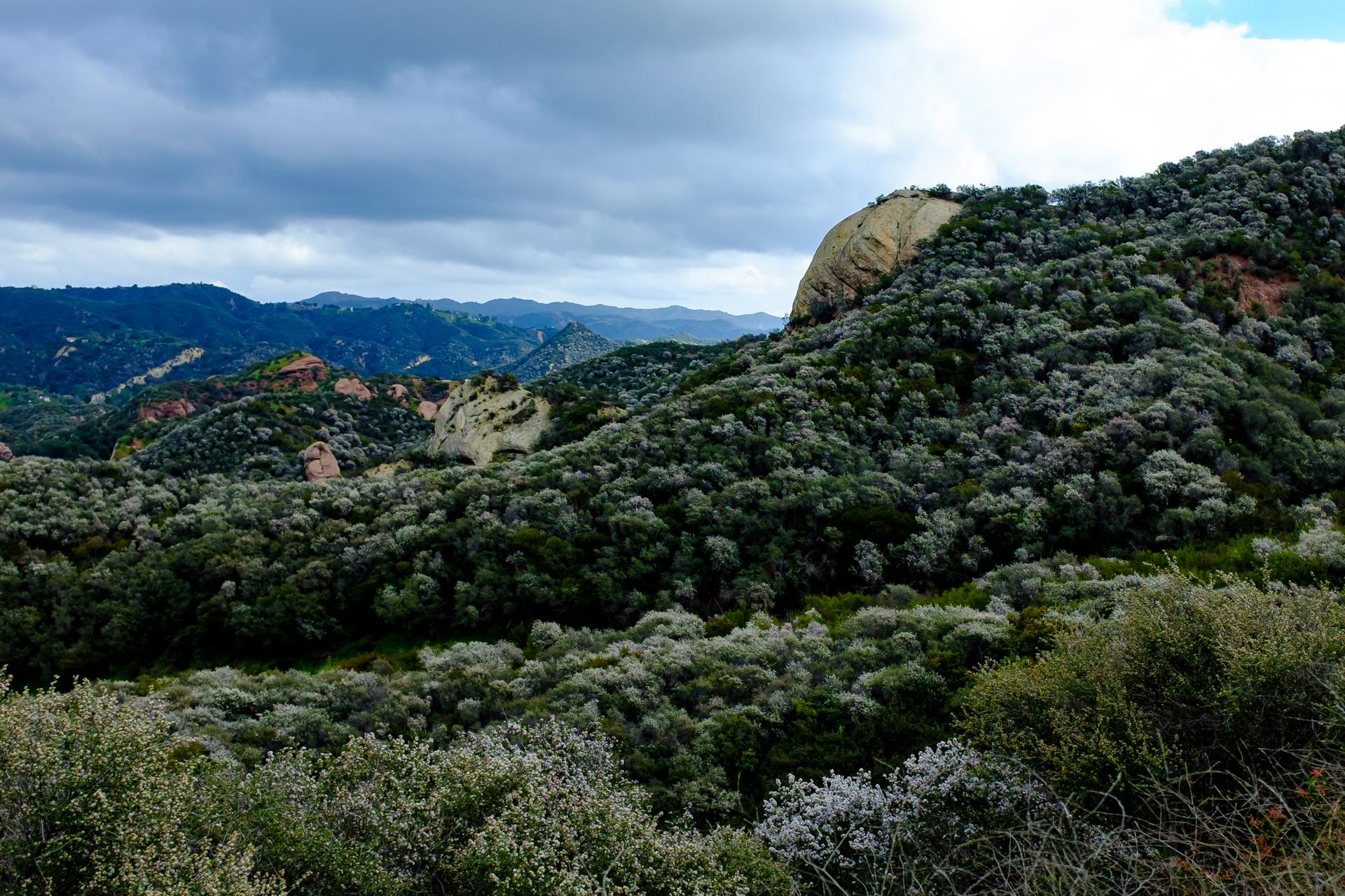 Dense green hills and rocky outcrops under a cloudy sky.