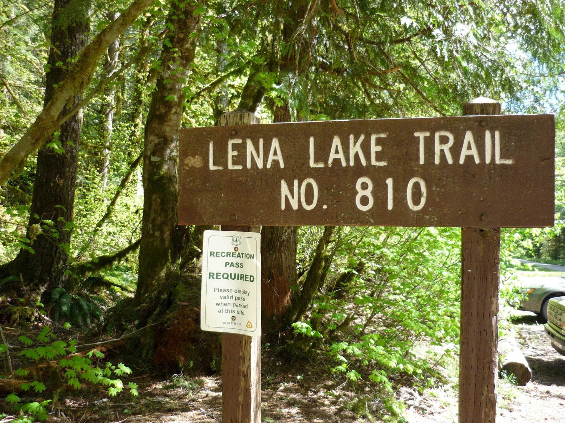 A brown wooden trail sign and smaller white sign in a sunlit forest.